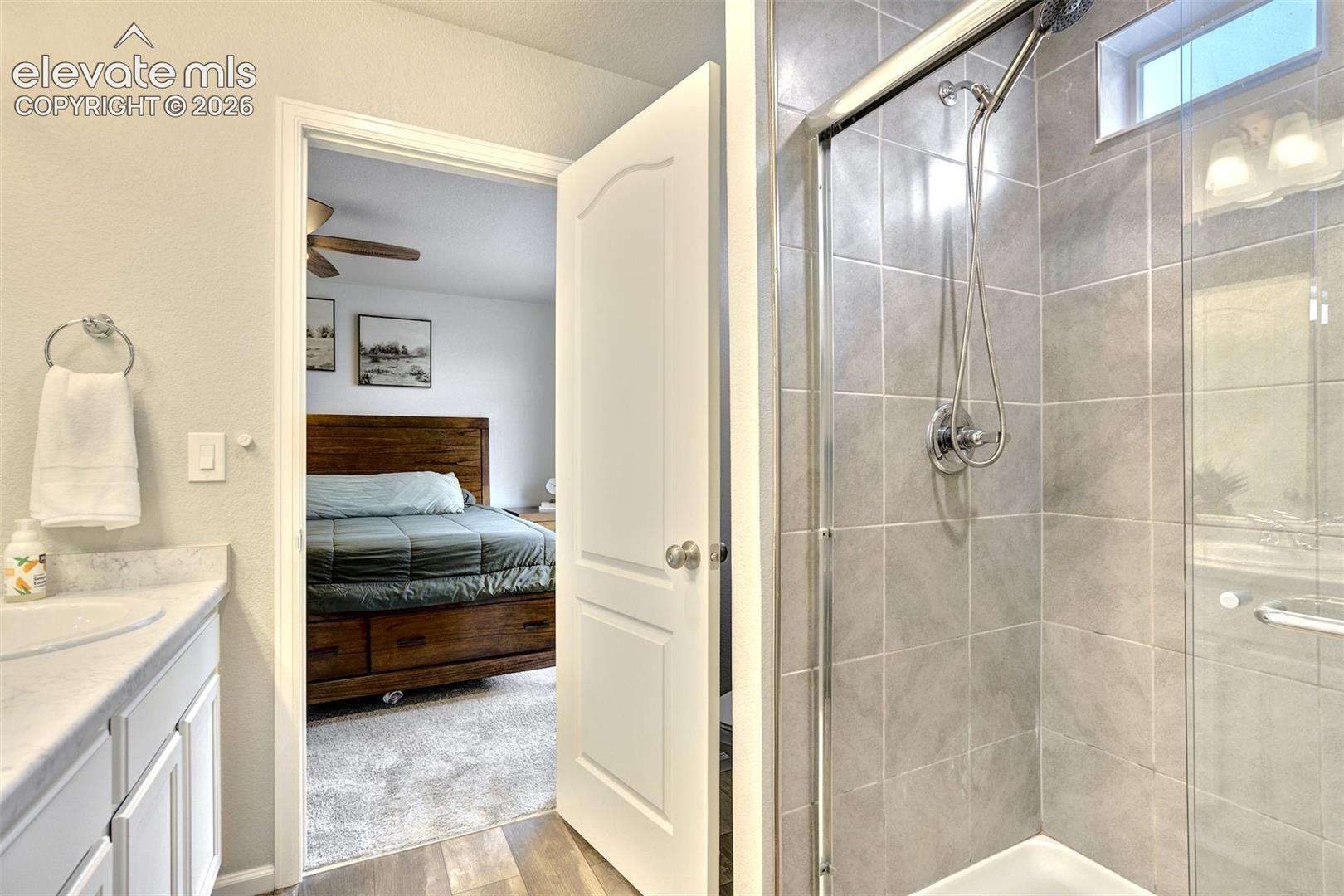 Bathroom vanity featuring a light-toned countertop with an integrated basin, white cabinetry, and a walk-in shower with floor-to-ceiling gray wall tiling, a glass enclosure, and a chrome hand-held shower fixture