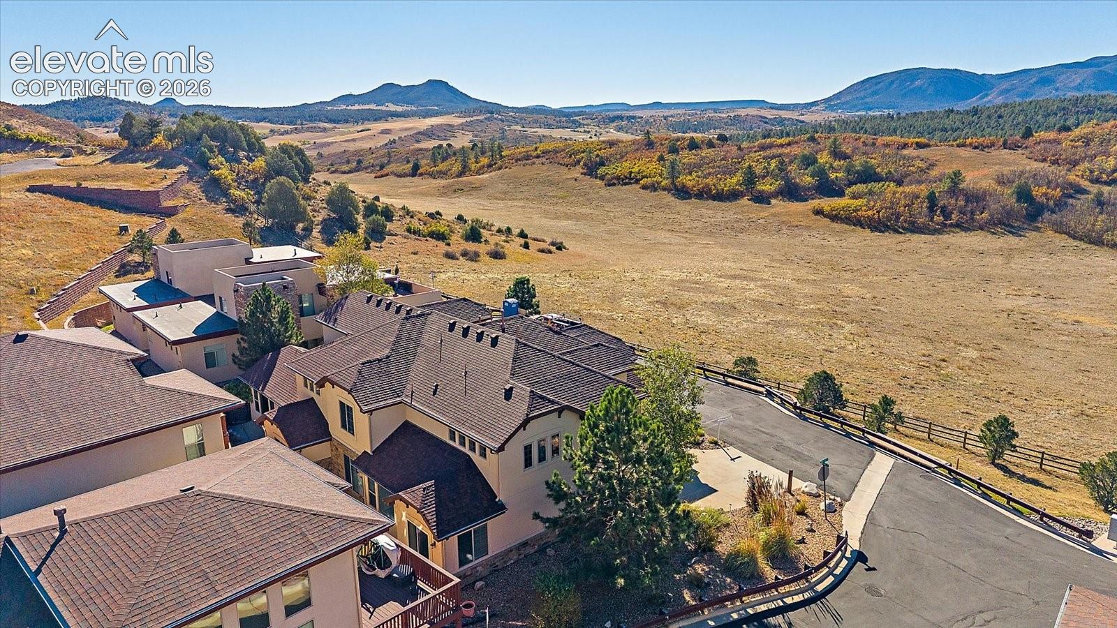 Multi-level stucco exterior with a composite shingle roof, asphalt driveway, and expansive open-space landscape featuring mountain topography