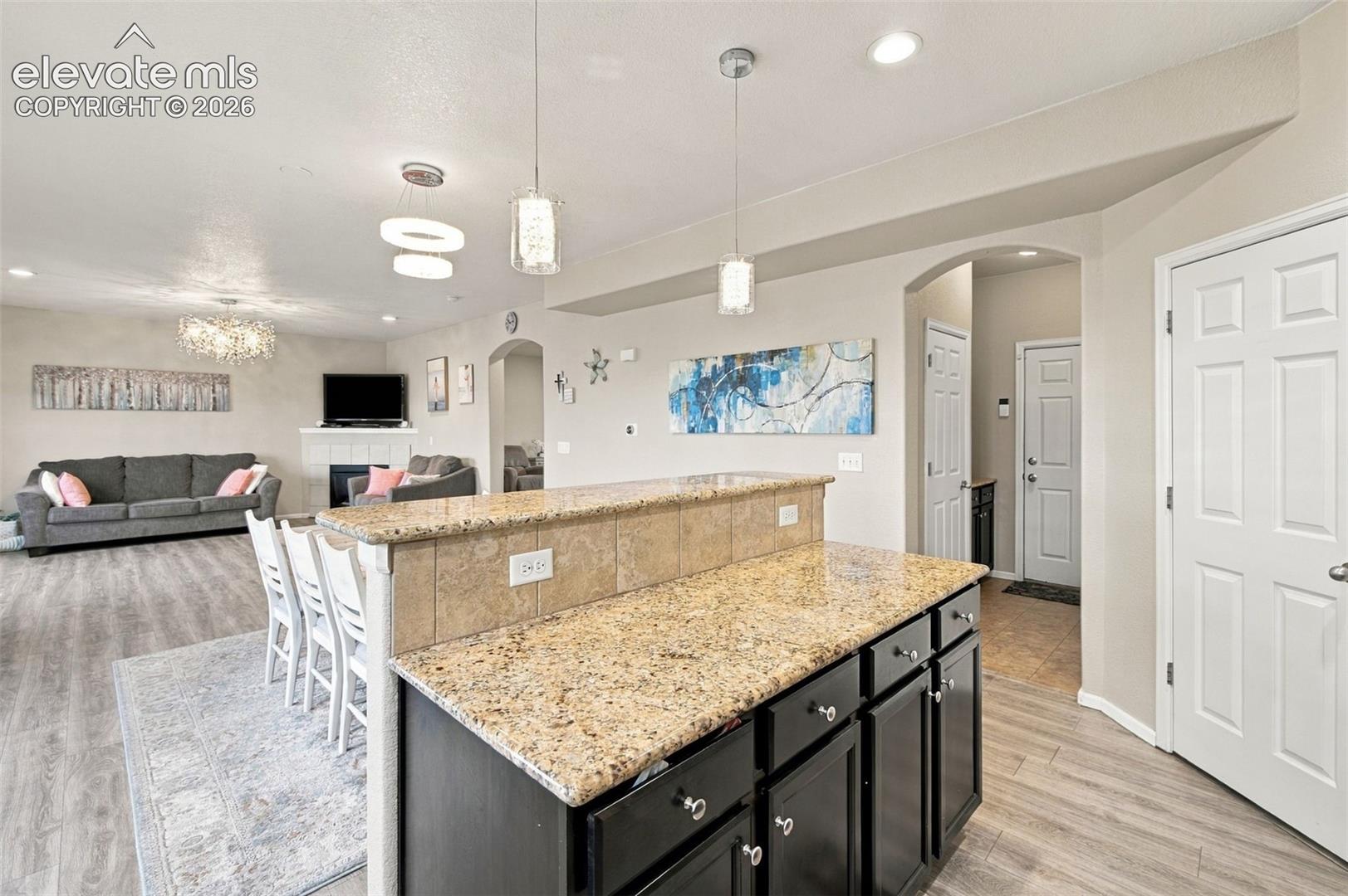 Kitchen island with stone-finish countertop, tiled backsplash, dark cabinetry, wood-finish flooring, and pendant lighting
