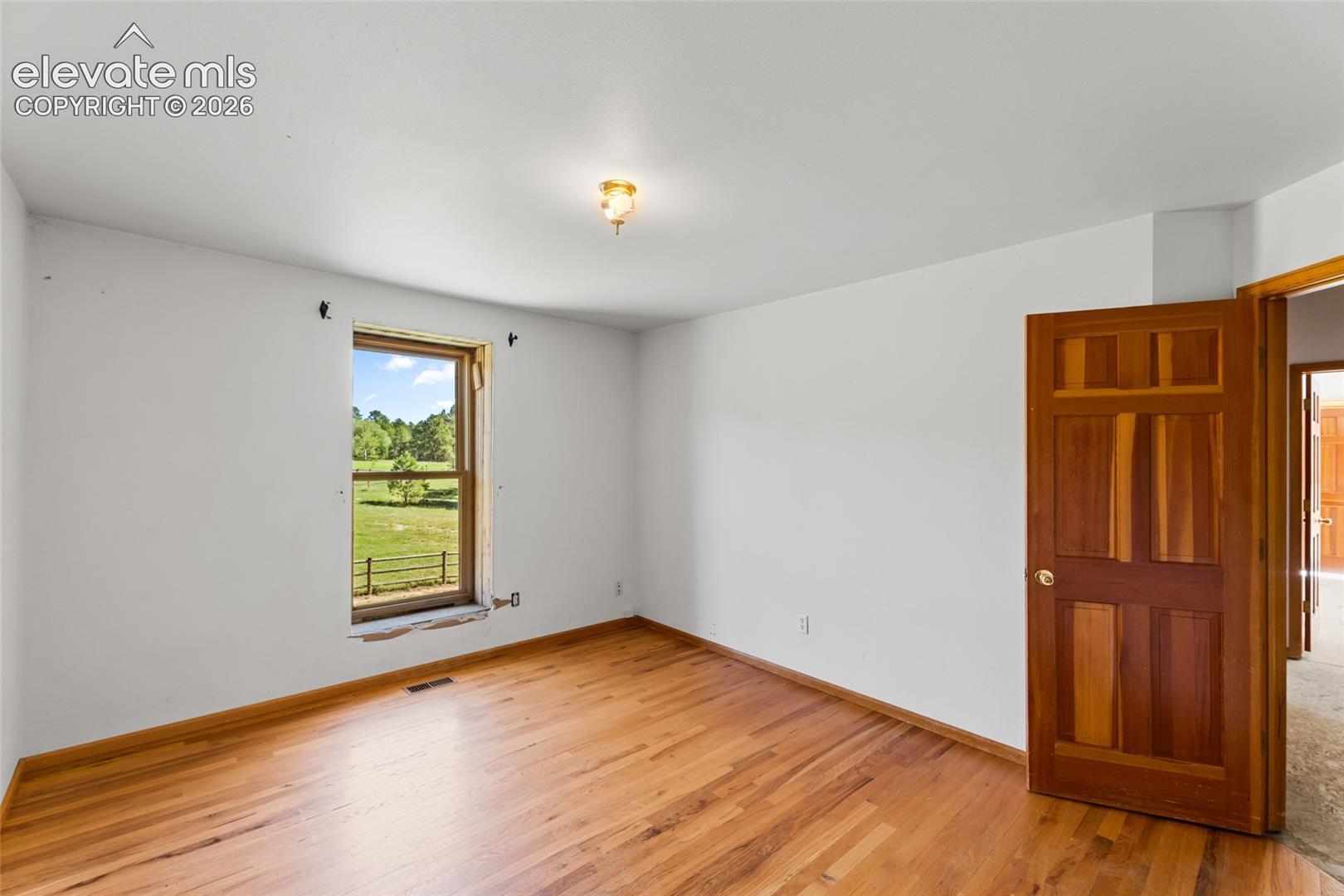 Hardwood flooring, painted white walls, wood panel interior door, and a single window with a country landscape