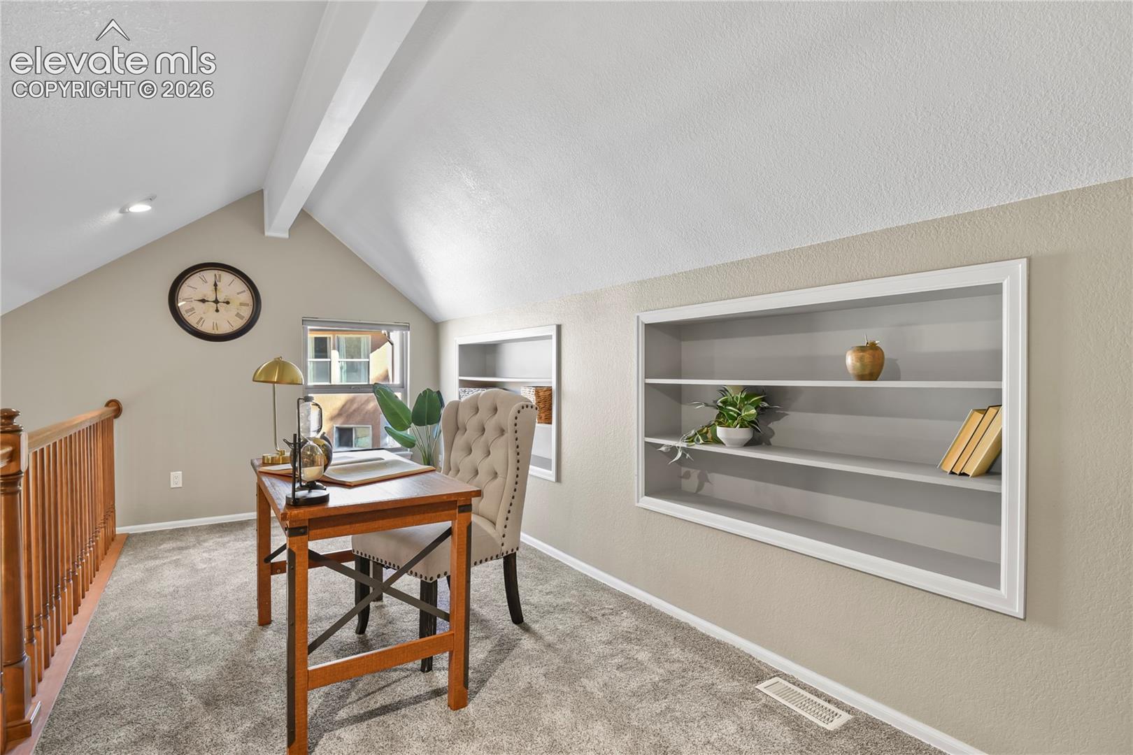 Vaulted ceilings featuring a prominent structural beam, built-in recessed shelving units with white casing, and a natural wood balustrade