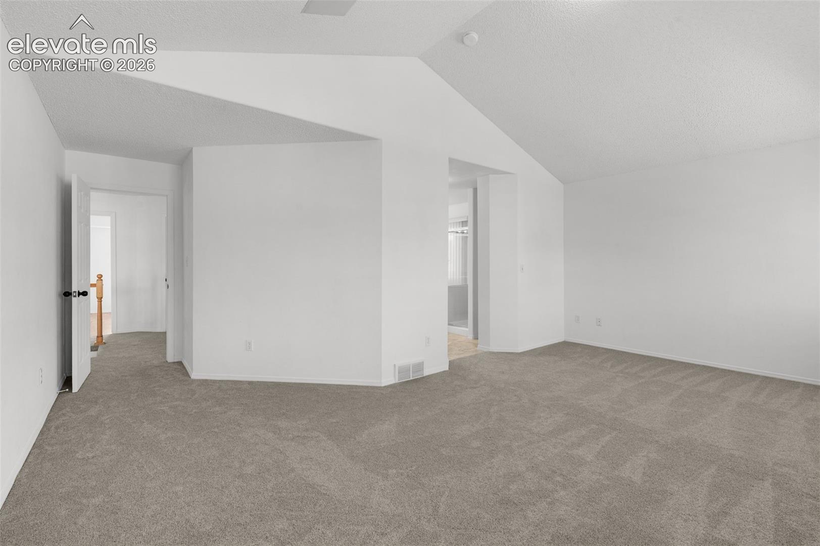 Neutral-toned carpeting, white walls, and a vaulted ceiling