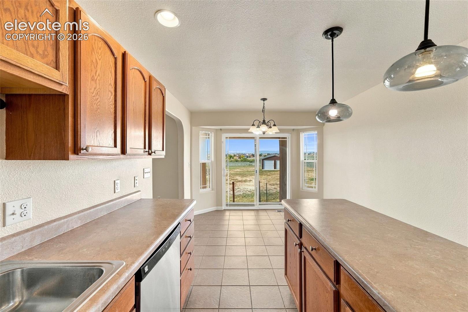 Kitchen featuring wood cabinetry, solid-surface countertops, tile flooring, recessed and pendant lighting, and glass sliding doors