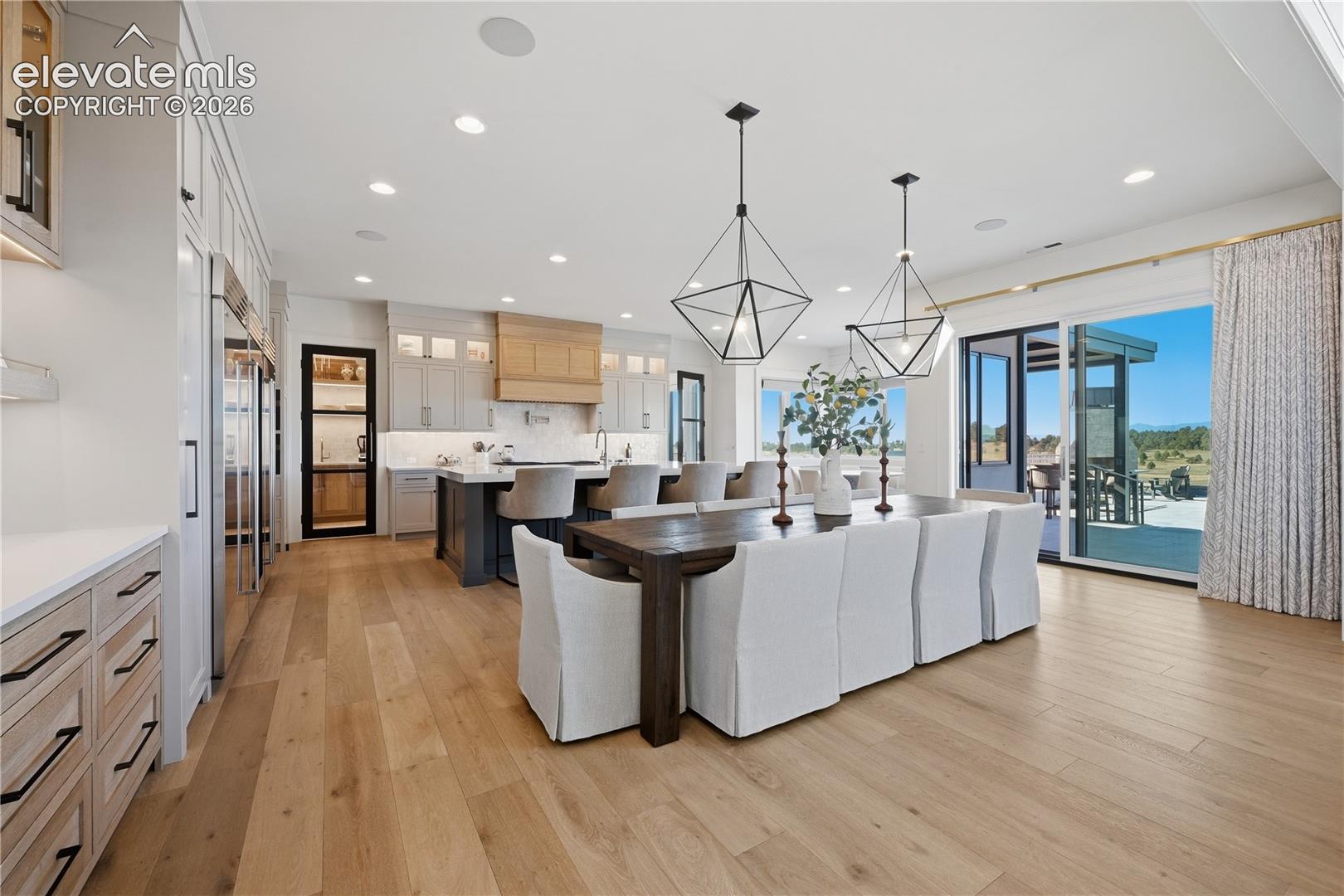 Open-concept kitchen featuring an expansive center island, custom built-in cabinetry, wood-finish flooring, geometric pendant lighting, and floor-to-ceiling glass sliding doors