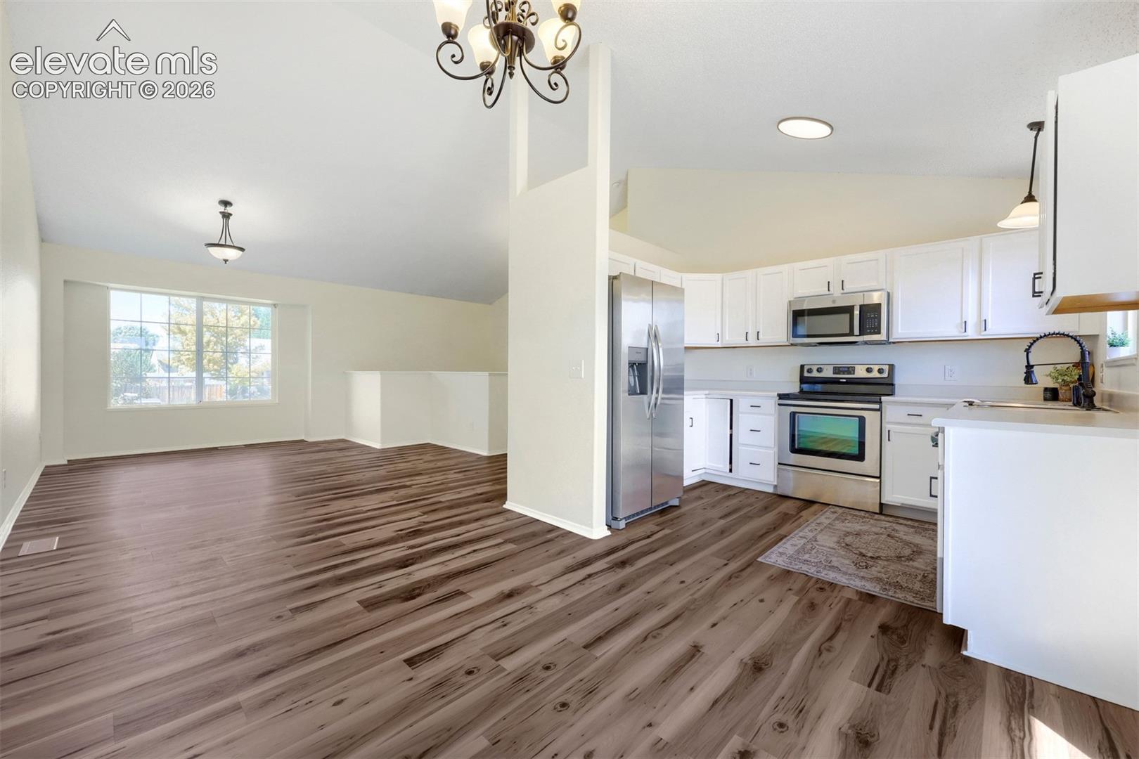 Vaulted ceilings, wood-finish flooring, white cabinetry, stainless steel appliances, and a large window
