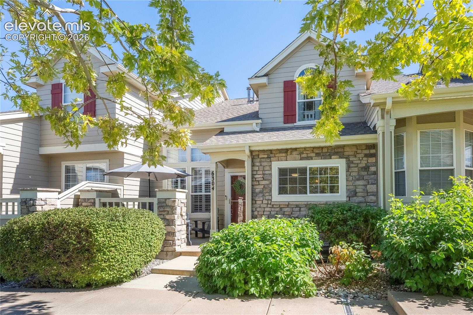 Multi-gabled exterior featuring horizontal siding, decorative stone veneer, red shutters, and arched window detailing