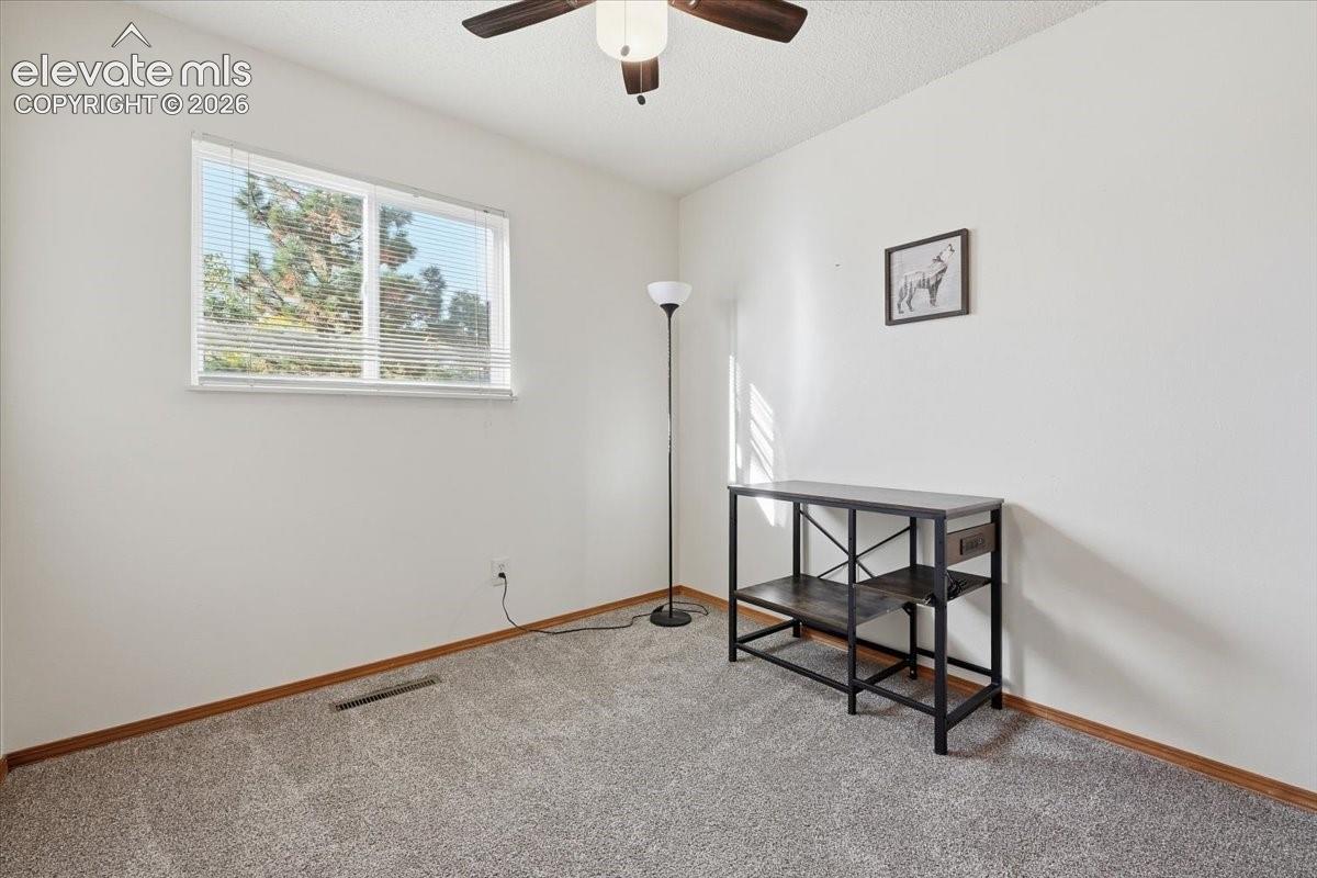 Recessed window with blinds, ceiling fan with integrated lighting, textured white walls, and gray carpeting