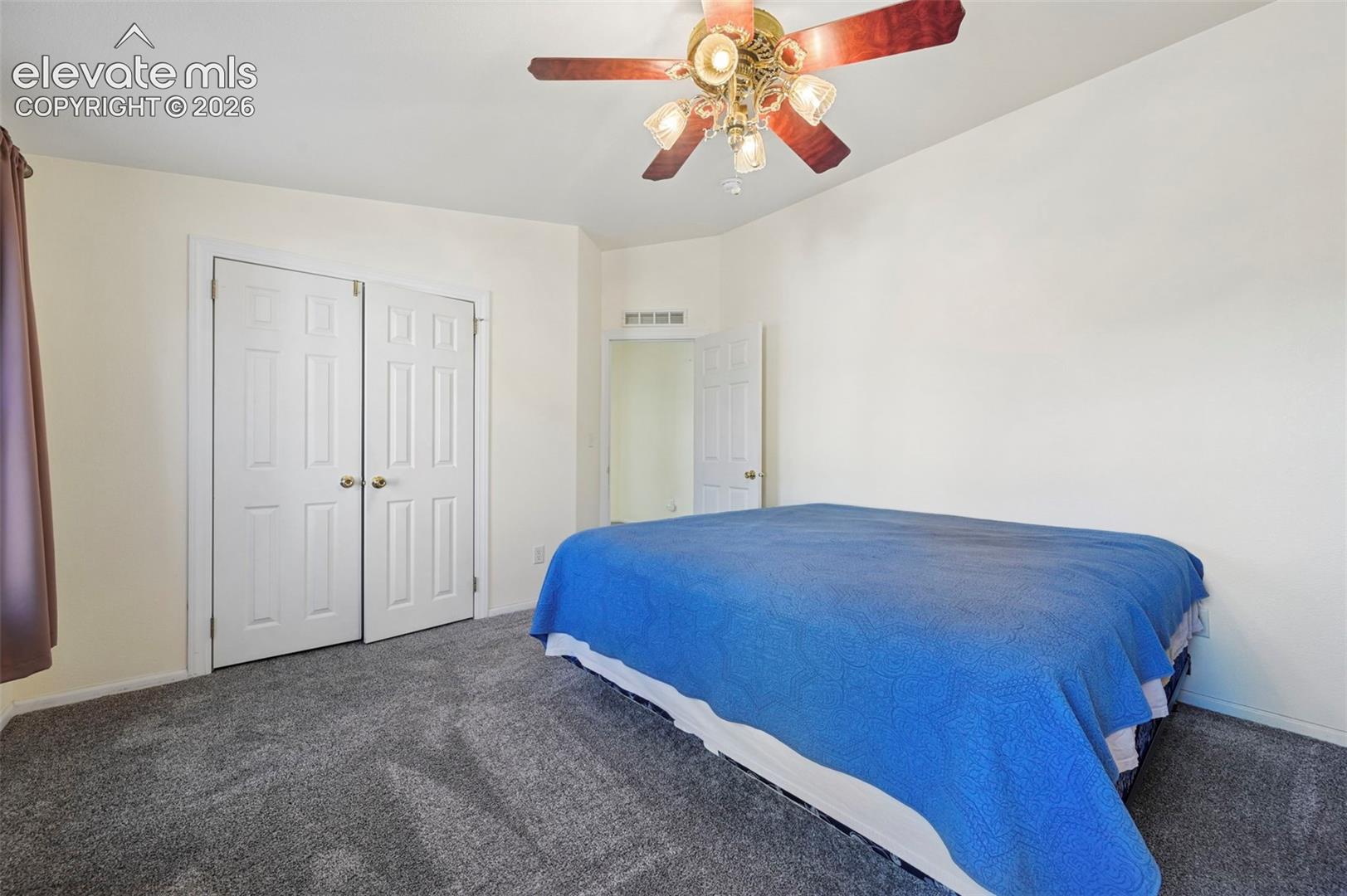 Neutral-toned wall finish, wall-to-wall carpeting, ceiling fan with integrated lighting, and a double-door closet