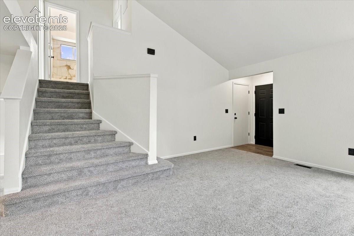 Staircase with carpeted steps and a white railing, featuring vaulted ceilings and neutral wall tones
