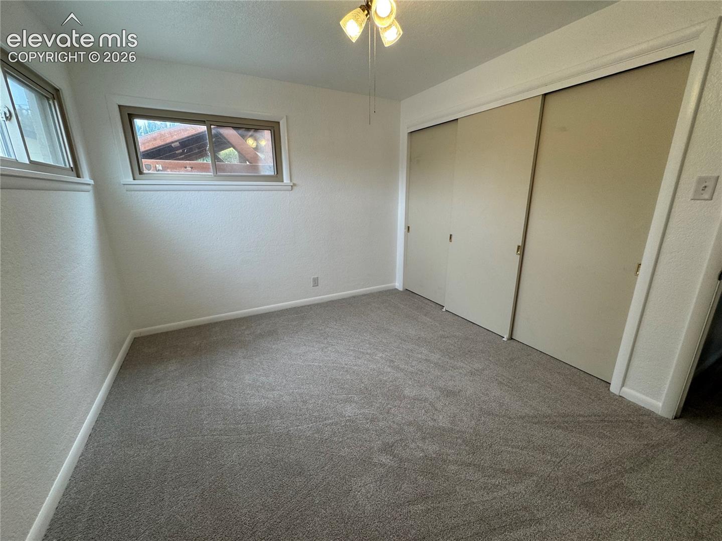 Bedroom featuring wall-to-wall carpeting, sliding-panel closet doors, dual-pane slider windows, and a three-light ceiling fixture