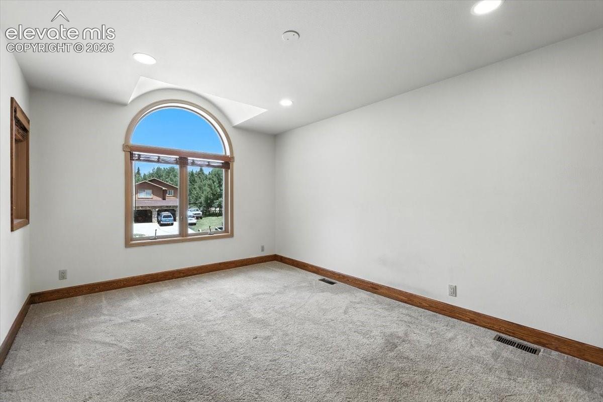 Interior space featuring a vaulted ceiling, arched window with wood trim, recessed lighting, and neutral carpeting