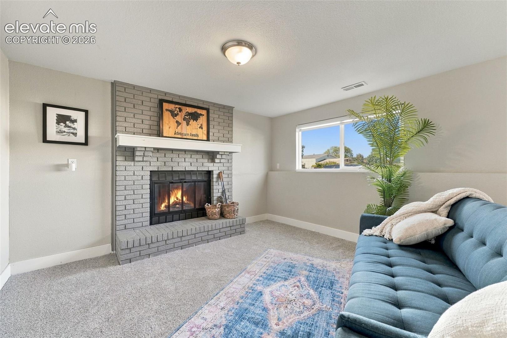 Recessed window with exterior scenery, light gray brick fireplace with a white mantel, and ceiling-mounted light fixture