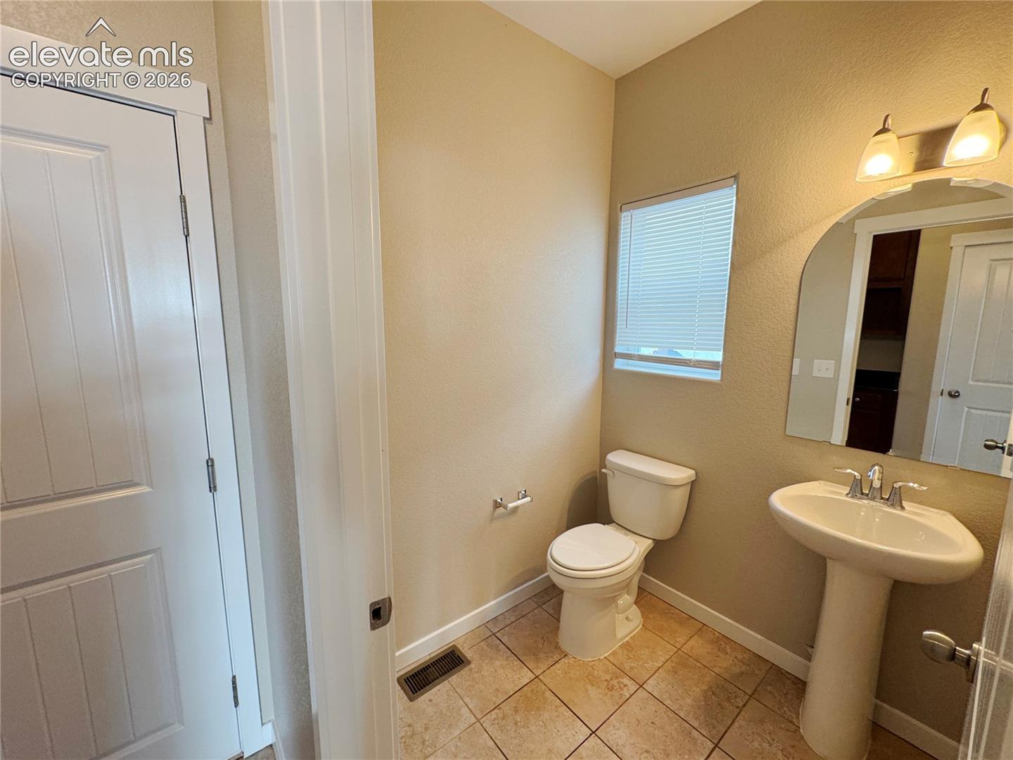 Pedestal sink with chrome faucet, arched wall mirror, two-light fixture, and ceramic tile flooring