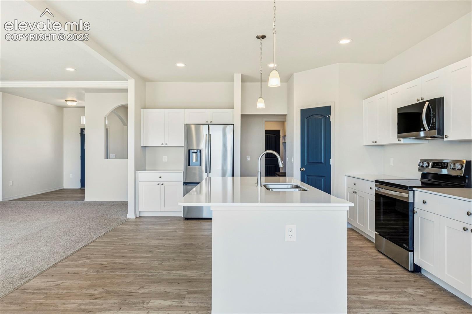 Modern kitchen featuring white cabinetry, stainless steel appliances, a center island with a sink, pendant lighting, and wood-finish flooring