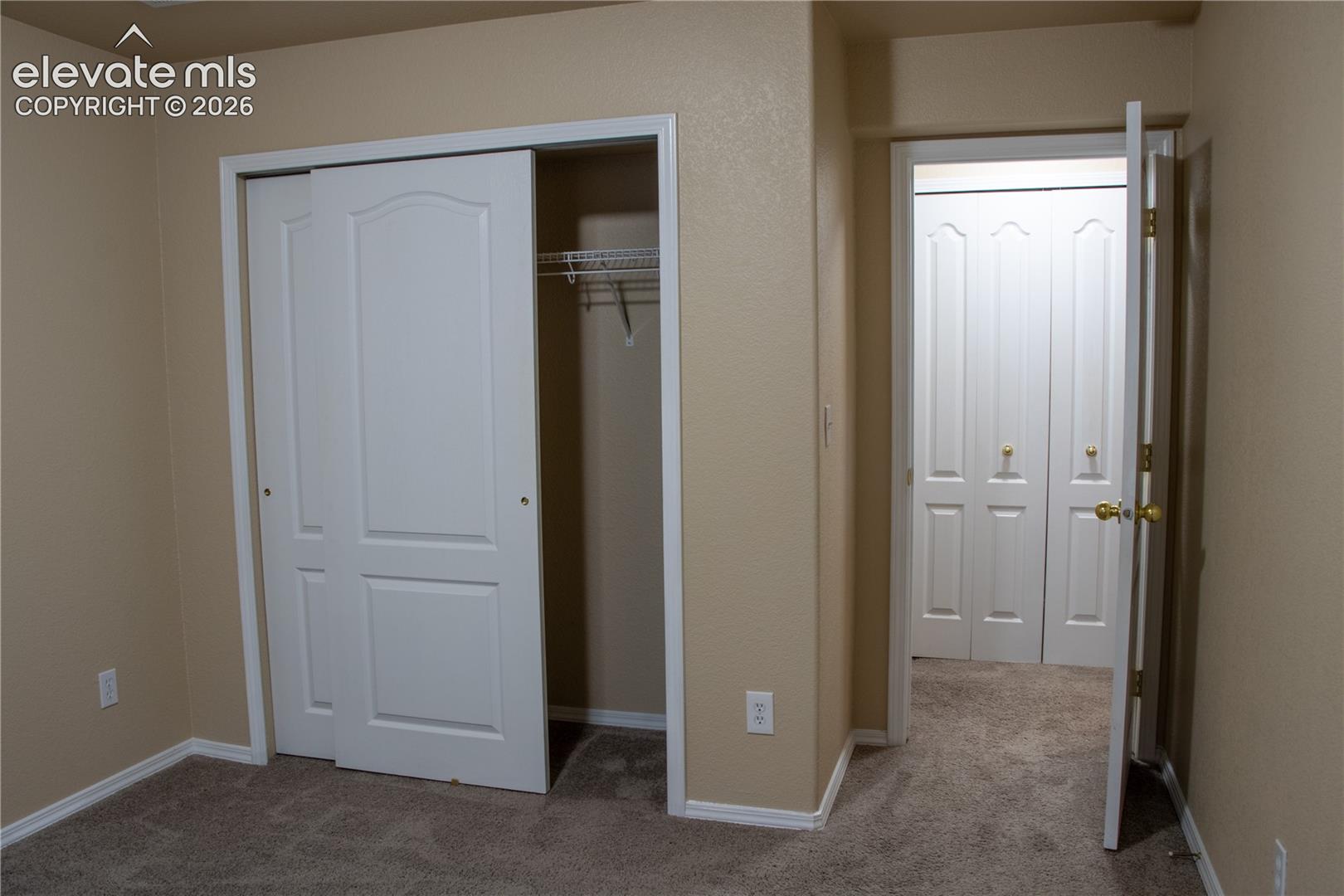 Room featuring neutral wall tones, textured carpeting, white baseboards, and a sliding two-panel closet door with wire shelving