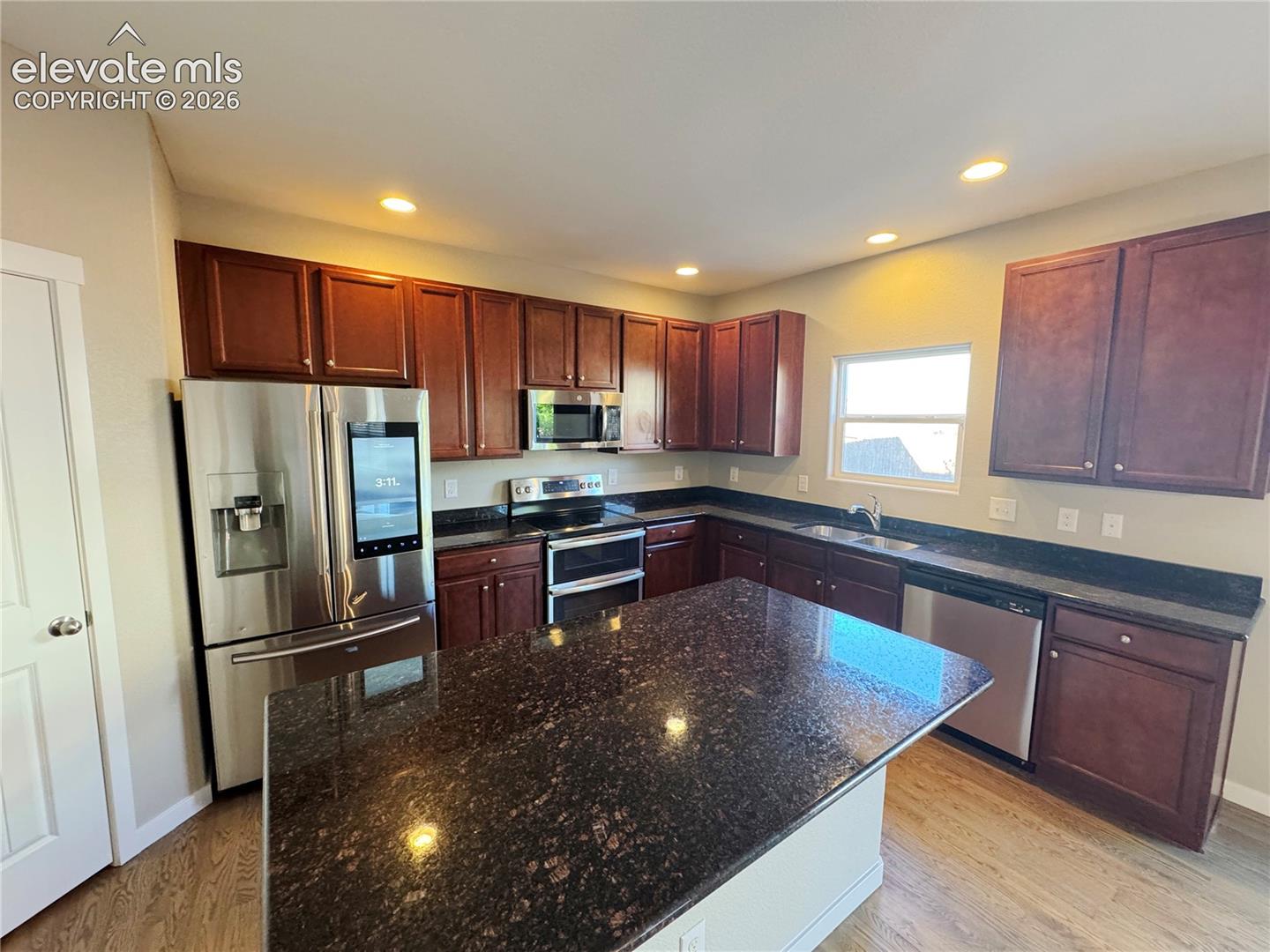 Kitchen featuring dark-toned cabinetry, a spacious center island with stone-finish countertops, stainless steel appliances, and wood-finish flooring