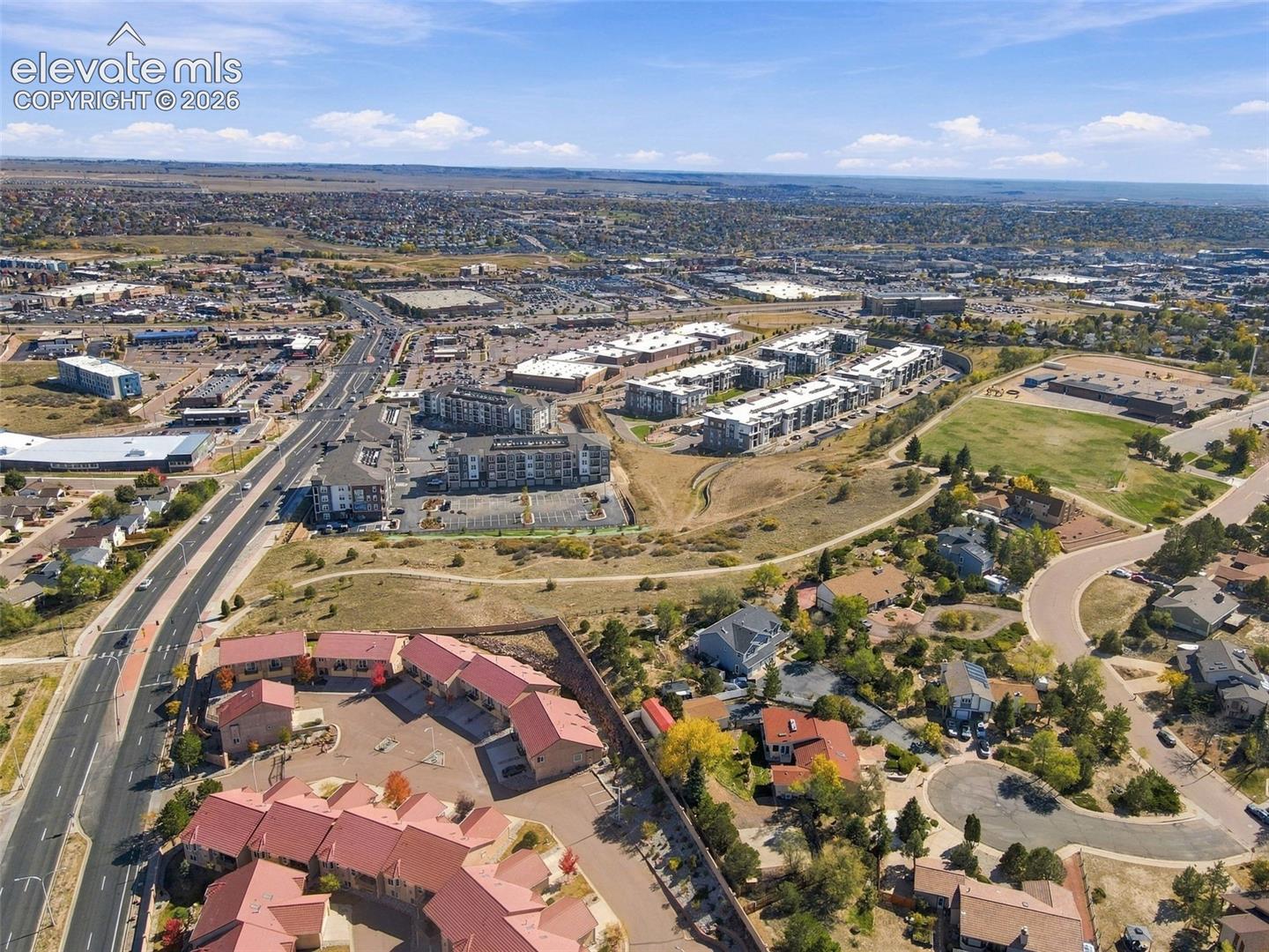 Aerial perspective of a multi-unit residential complex featuring red shingle roofing, paved surface parking, and exterior stone and siding finishes