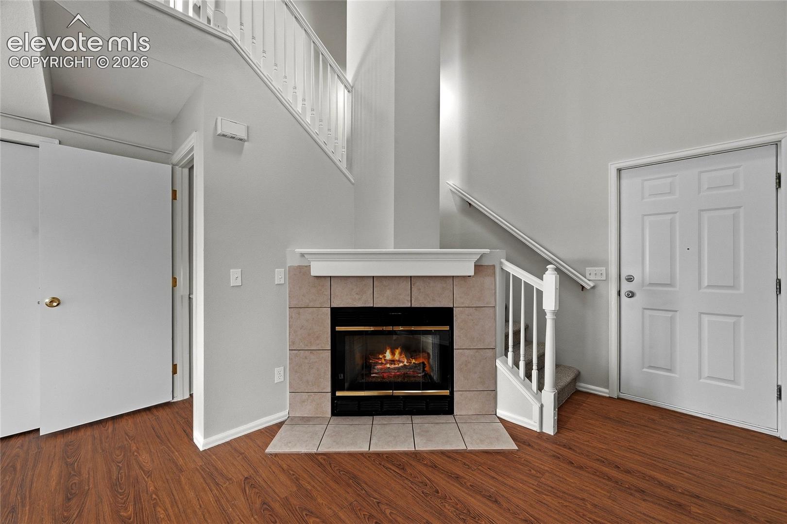 Two-story entry area featuring wood-finish flooring, a fireplace with a ceramic tile surround and mantel, and a staircase with white balusters