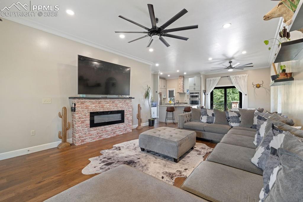 Living area with wood finished floors, ornamental molding, ceiling fan, a fireplace, and recessed lighting
