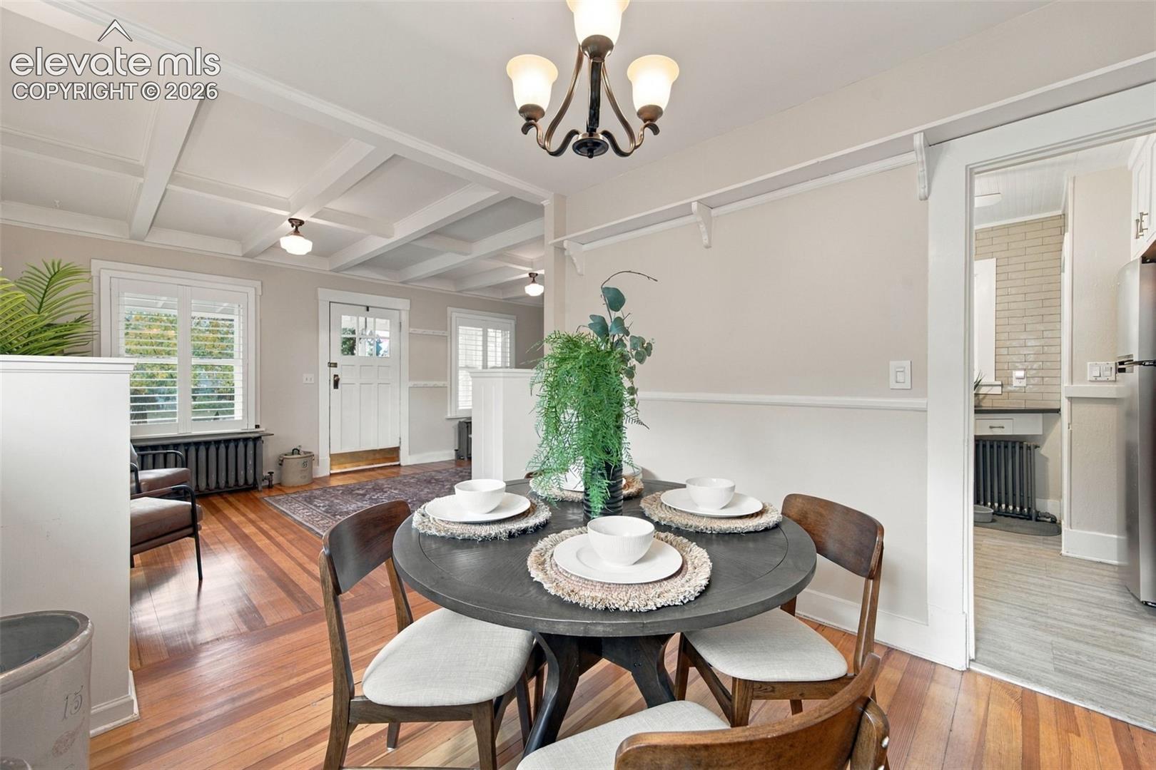 Dining area featuring coffered ceilings, original wood-finish flooring, and a multi-arm light fixture, punctuated by white shutter window treatments and a classic radiator