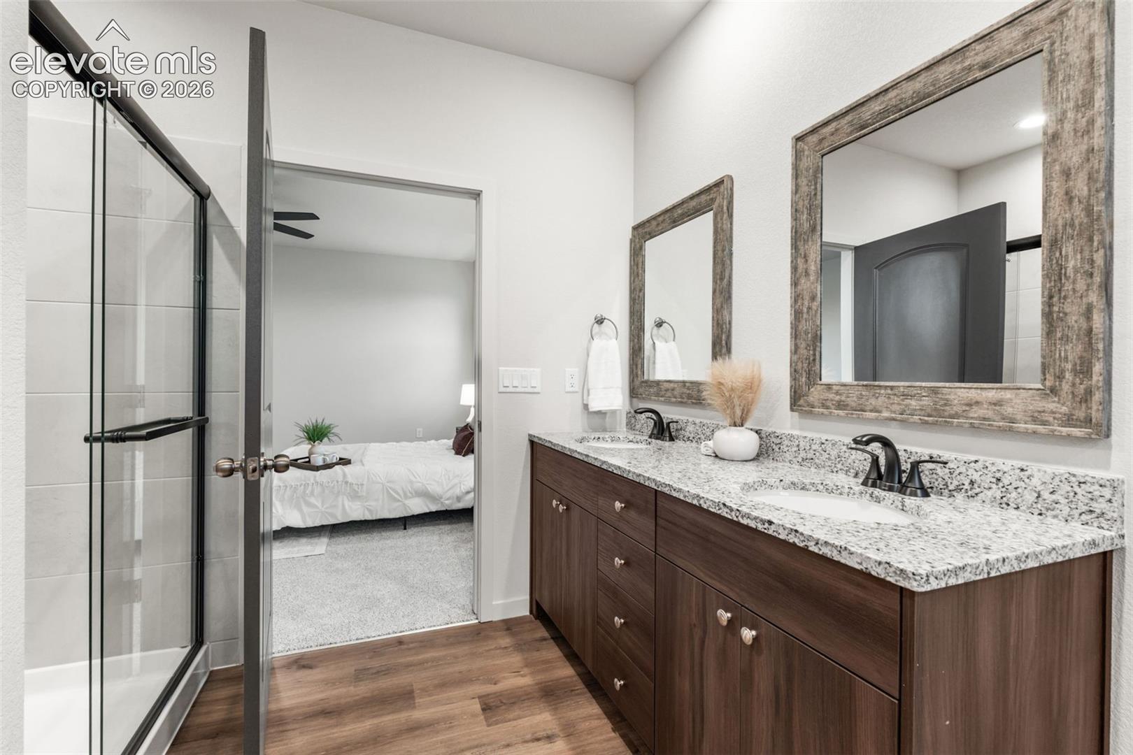 Bathroom featuring a dual-sink vanity with stone-patterned countertops, dark wood-finish cabinetry, walk-in shower with glass enclosure, and framed vanity mirrors