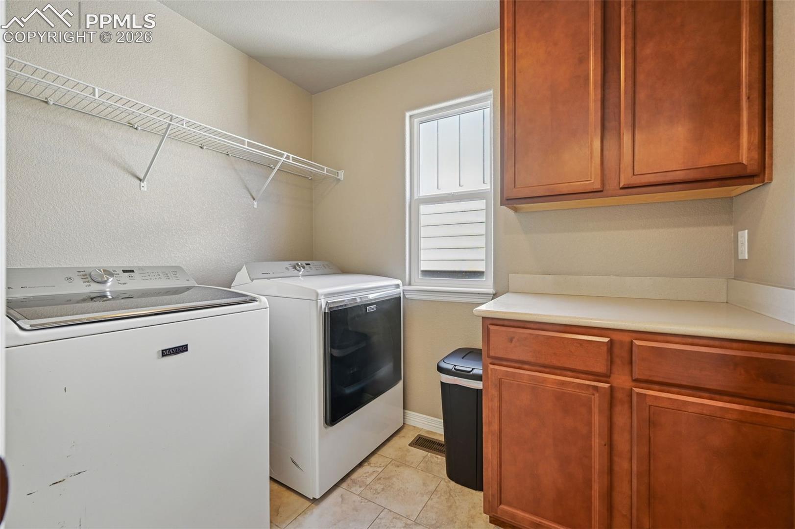 Laundry room with cabinet space, independent washer and dryer, a textured wall, and light tile patterned flooring