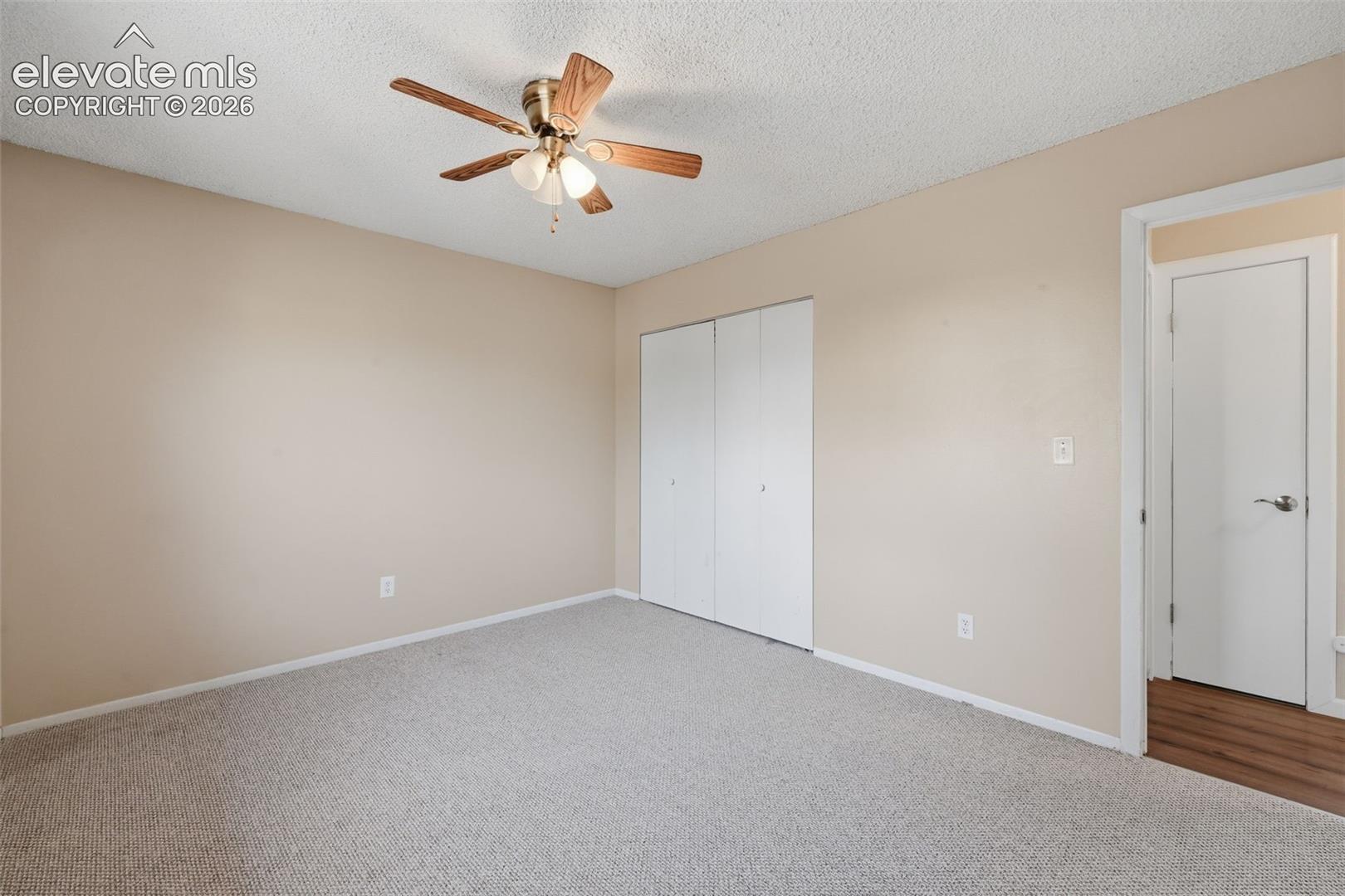 Neutral tone wall paint, textured ceiling, ceiling fan with integrated lighting, carpet flooring, and a white bi-fold closet
