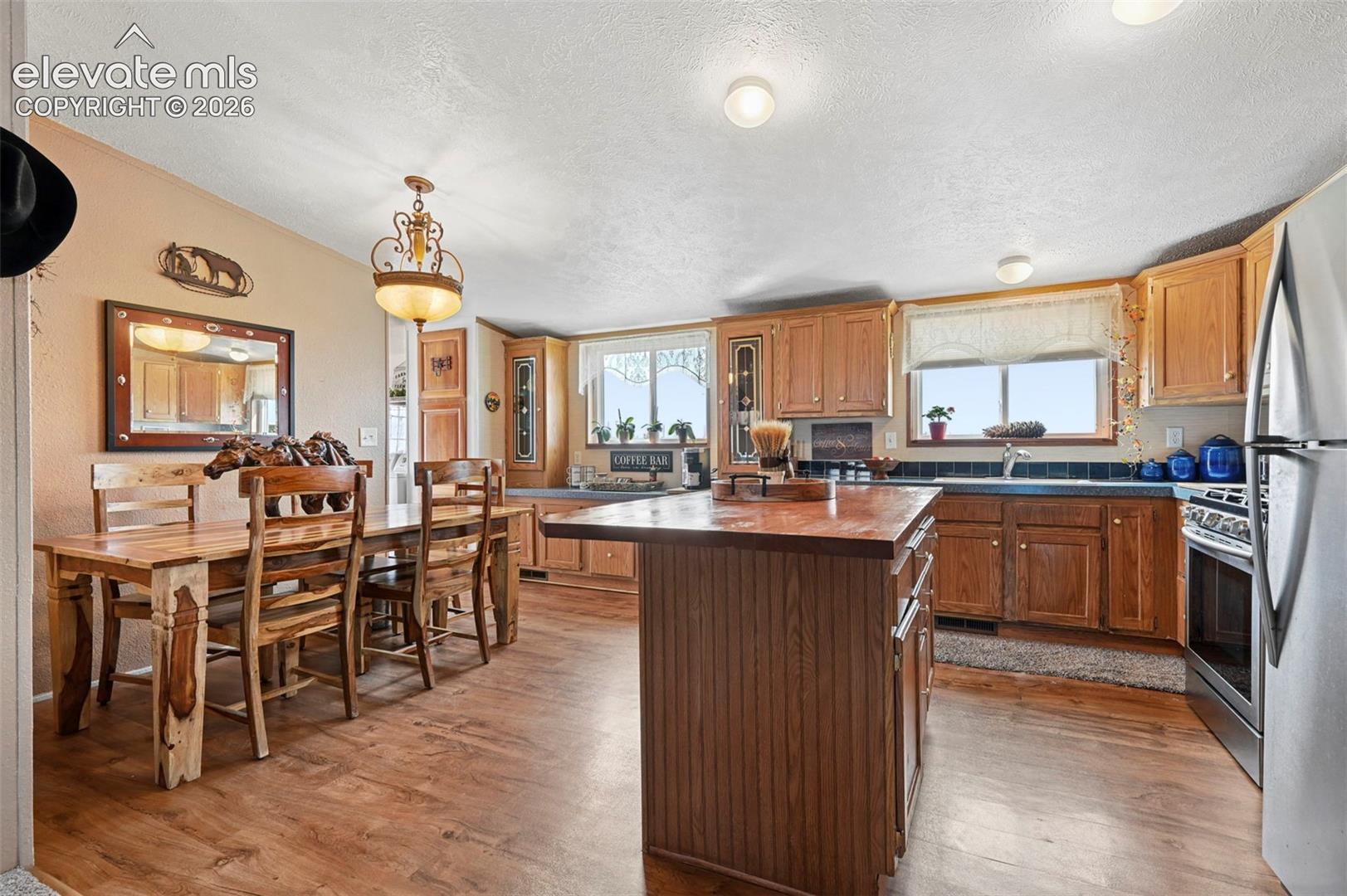 Kitchen featuring natural wood cabinetry, central island with butcher block countertop, wood-finish flooring.