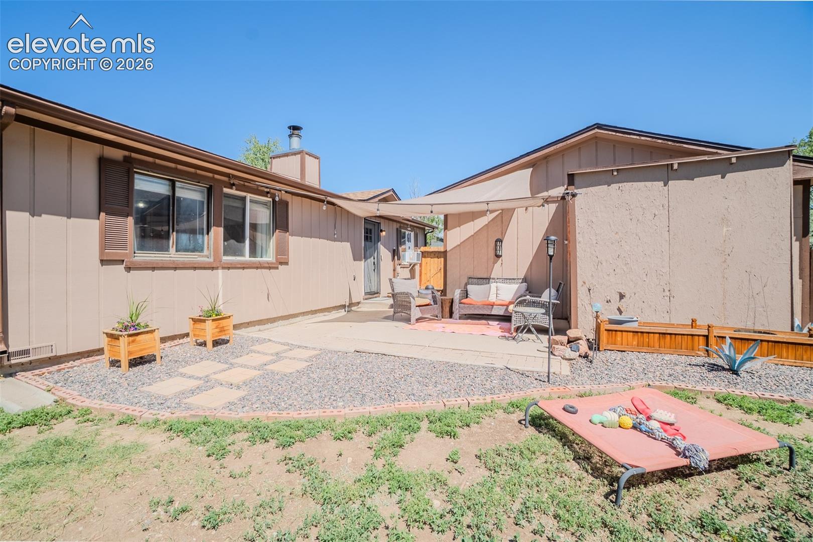 Outdoor patio area featuring a shade sail, concrete pavers, and decorative gravel