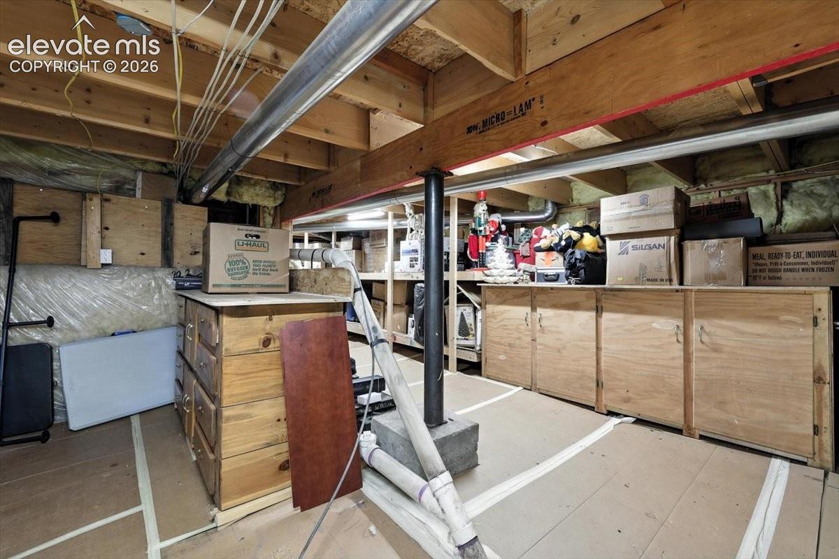 Unfinished storage space featuring exposed wooden structural framing, a structural steel support column, built-in wooden cabinetry, and taped subflooring