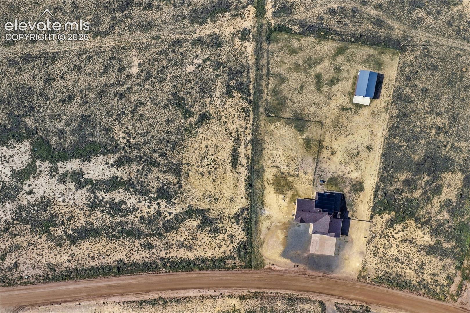 Aerial perspective of a sprawling property featuring a primary residence with a dark-toned shingle roof, a detached outbuilding, and expansive acreage