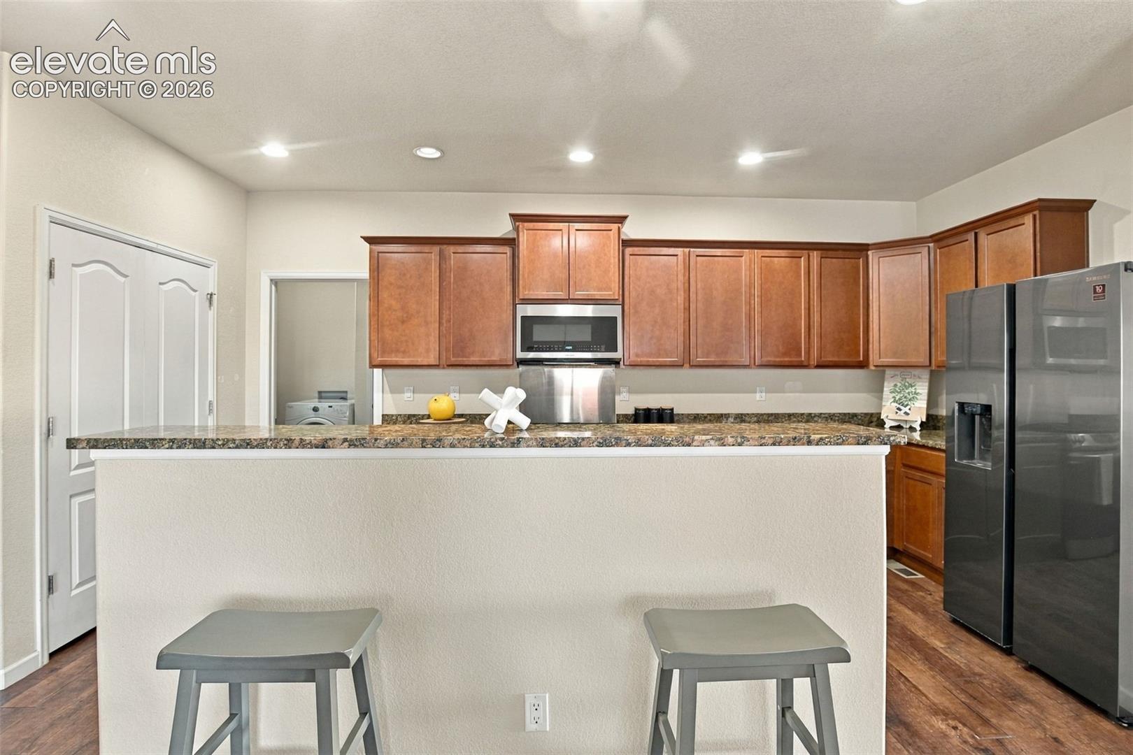Kitchen featuring wood cabinetry, stone countertops, stainless steel appliances, and wood-finish flooring