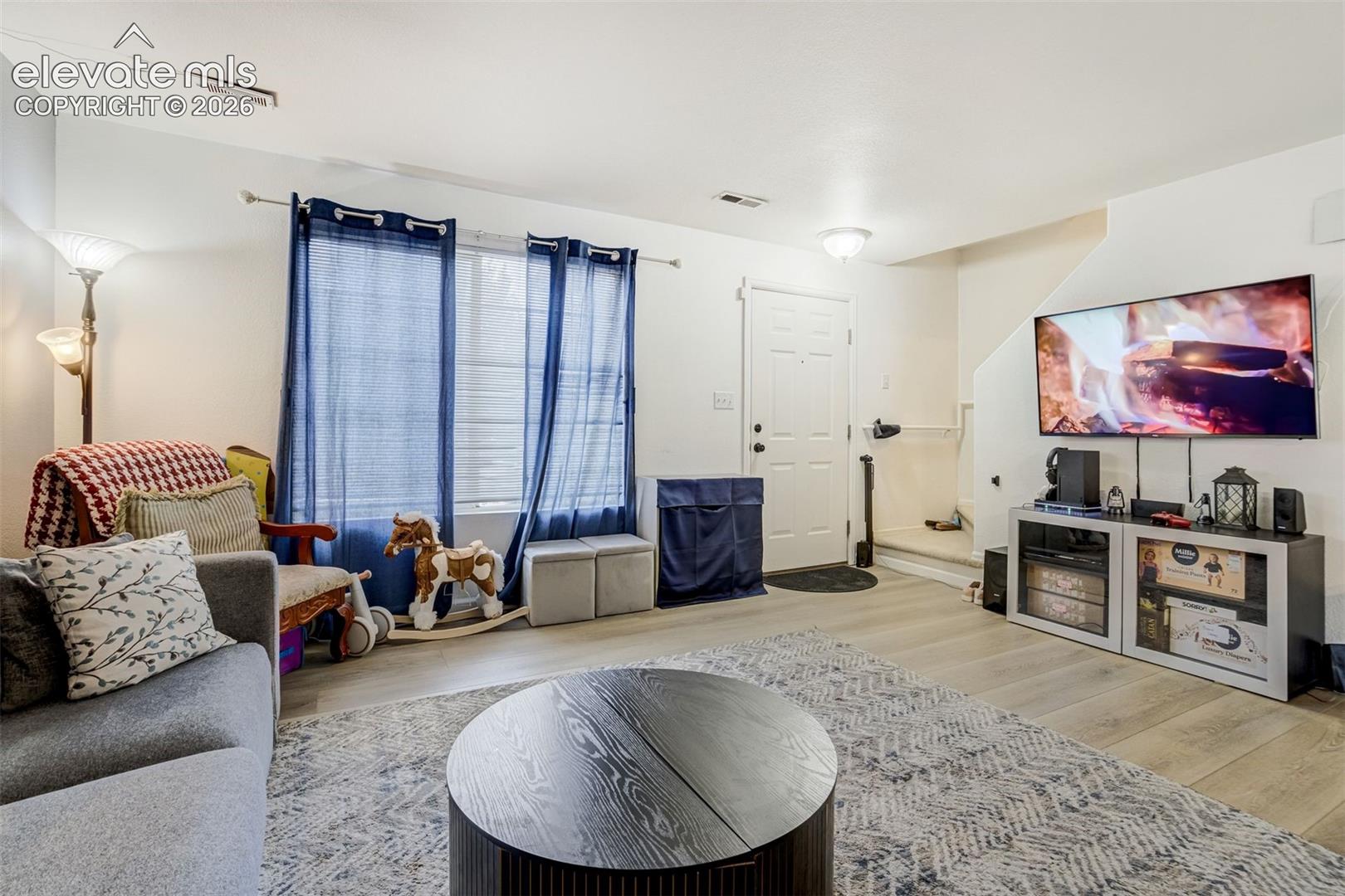 Spacious living area featuring light wood-finish flooring, white walls, and a white entry door