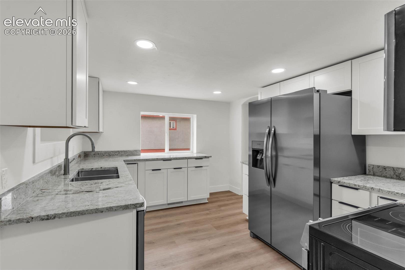 Kitchen featuring white shaker-style cabinetry, stone-finish countertops, stainless steel appliances, recessed ceiling lighting, and wood-finish flooring