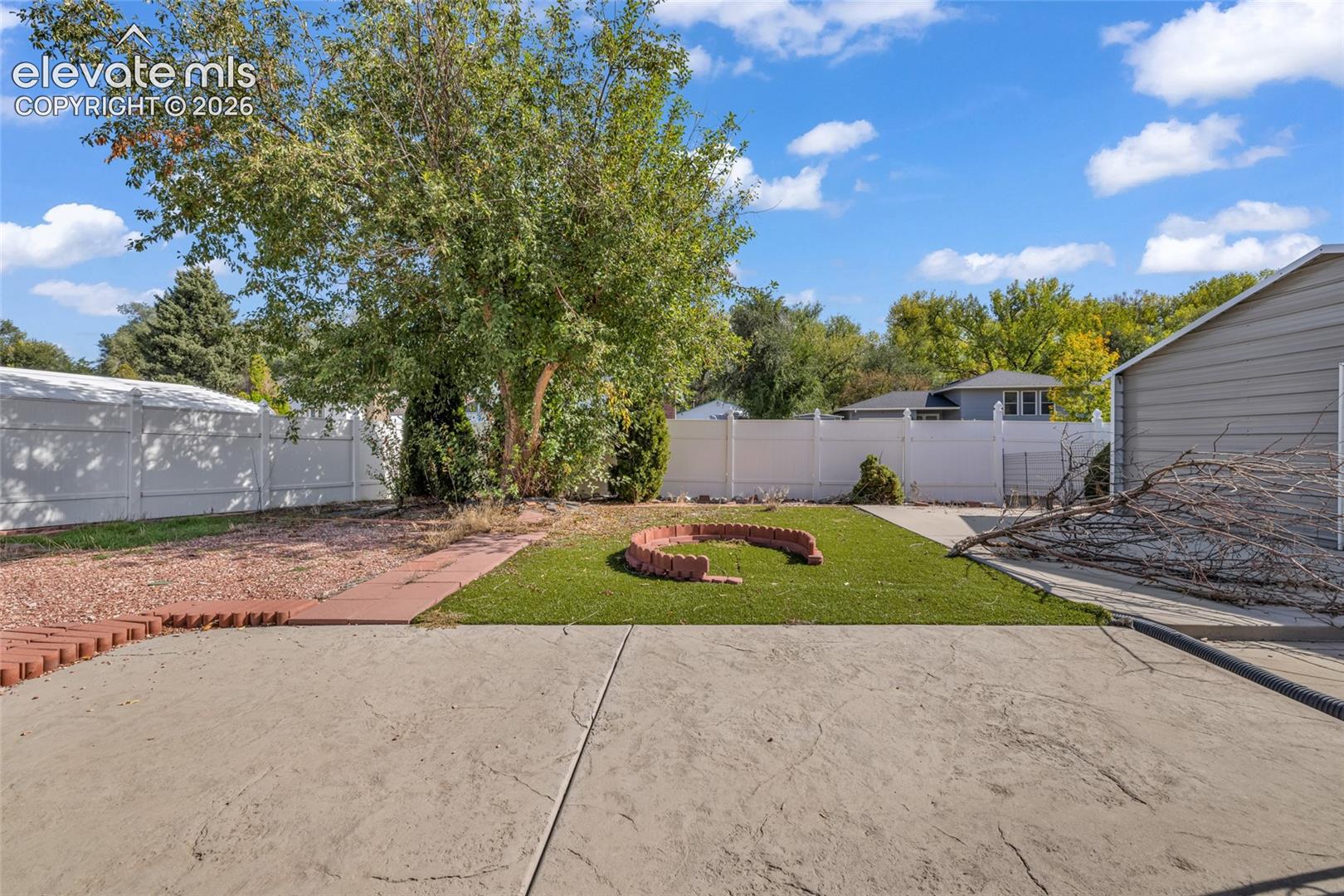 Expansive concrete patio leading to an artificial turf area with a brick-edged fire pit