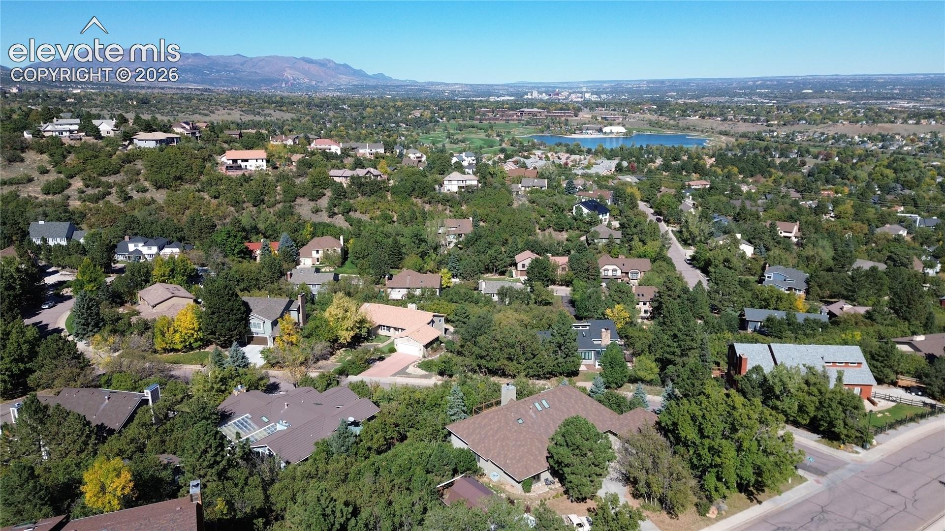 Aerial perspective featuring mature tree canopy, mountain range backdrop, and distant water feature