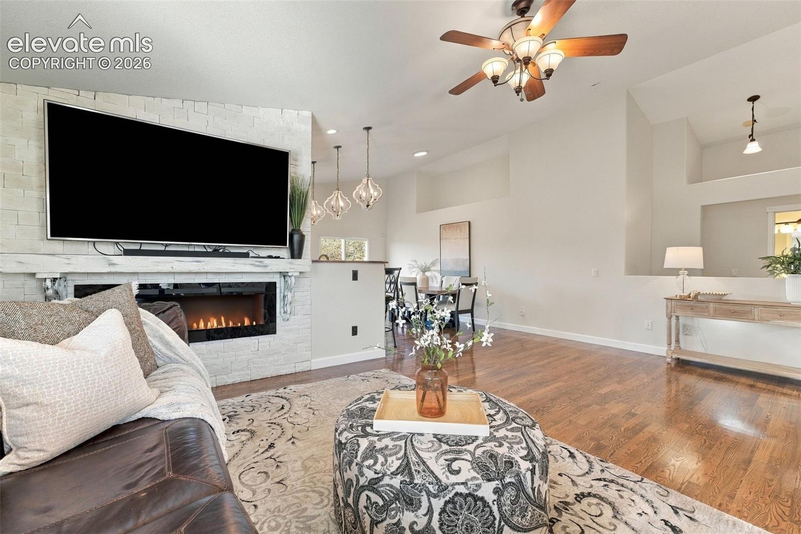 Living area featuring high ceilings, wood-finish flooring, a stacked-stone fireplace surround with a linear electric hearth, and custom recessed lighting