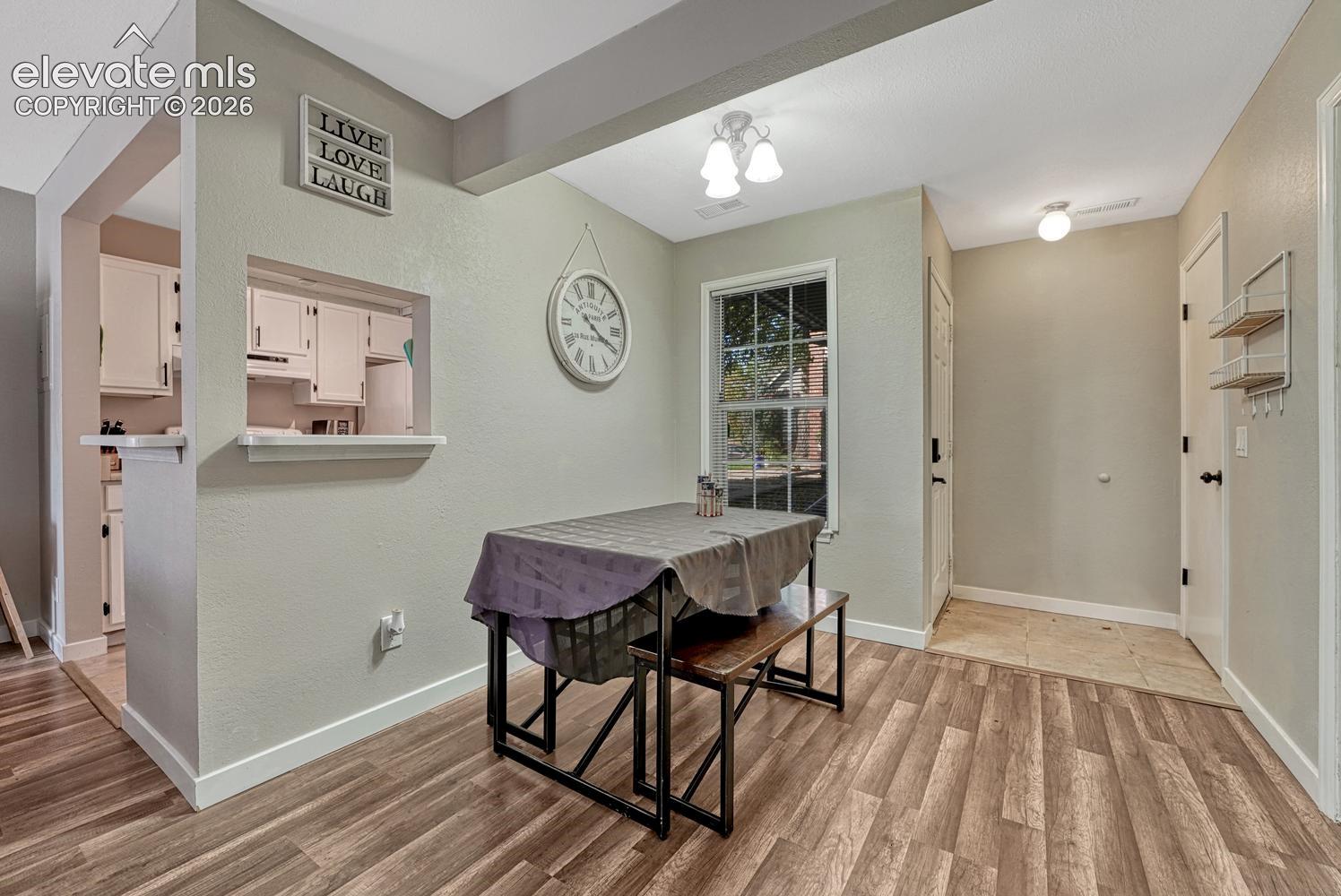 Wood-finish flooring, pass-through window to kitchen, white cabinetry, ceiling-mounted light fixtures, and a front entry door with transom