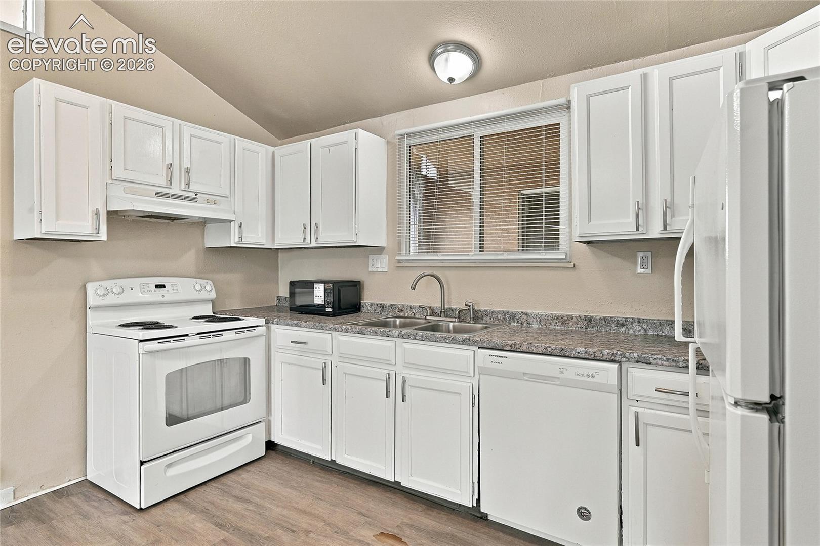 Kitchen featuring white cabinetry, stone-finish countertops, stainless steel dual-basin sink, and wood-finish flooring