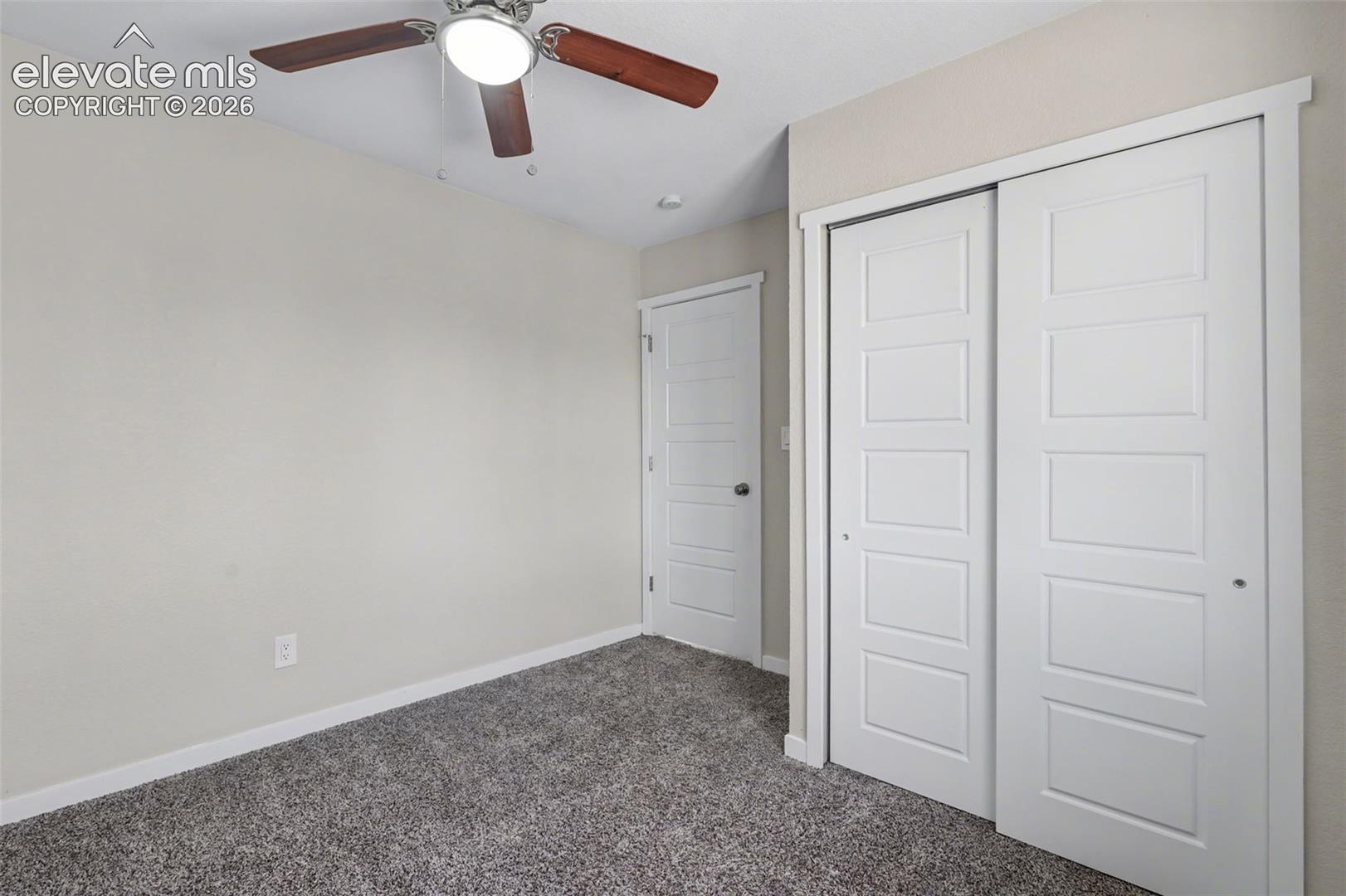 Neutral-toned interior featuring textured carpeting, five-panel interior doors, a sliding-door closet, and a ceiling-mounted fan with integrated light