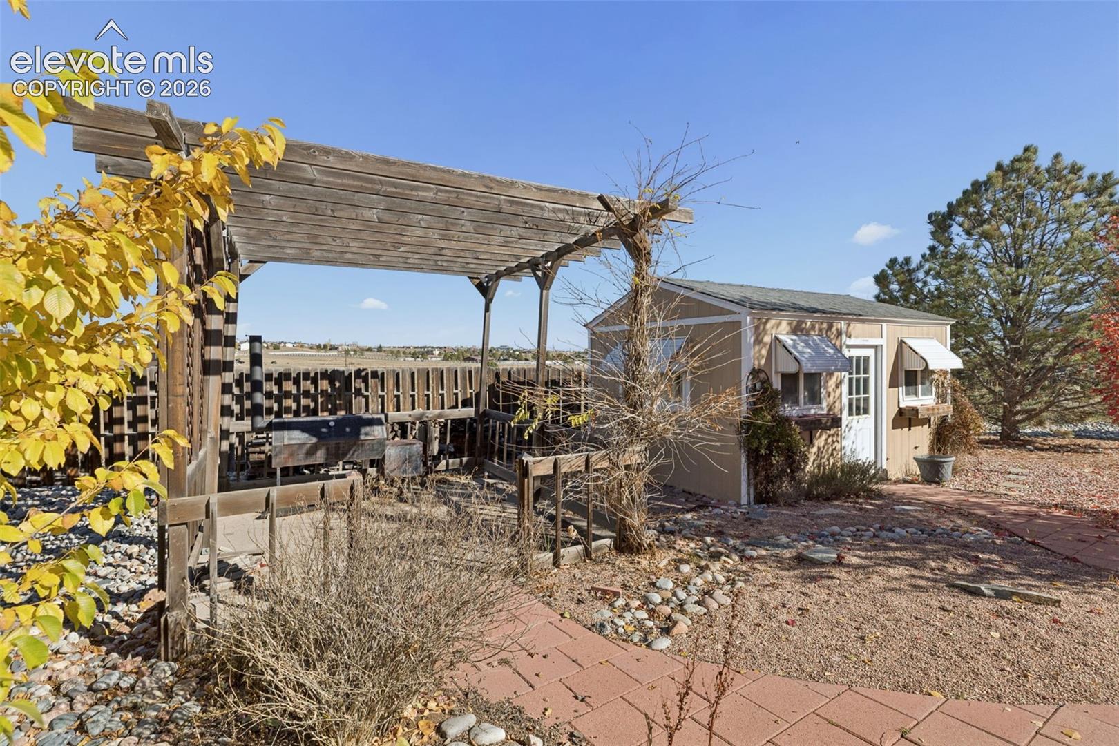 Outdoor space featuring a timber pergola, detached storage structure, paver walkway, and stone landscaping