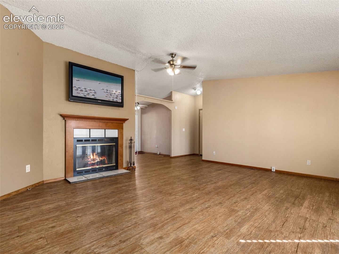 Fireplace with a wooden mantel, wood-finish flooring, vaulted ceilings, and a ceiling fan