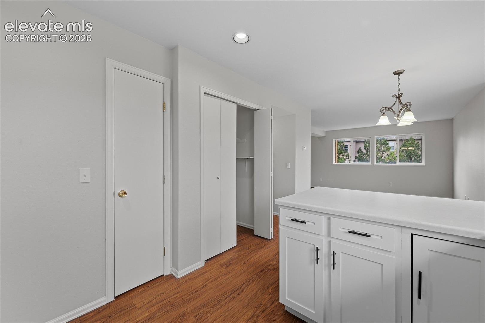 White cabinetry with matte black hardware, solid surface countertops, recessed lighting, multi-pane windows, and wood-finish flooring