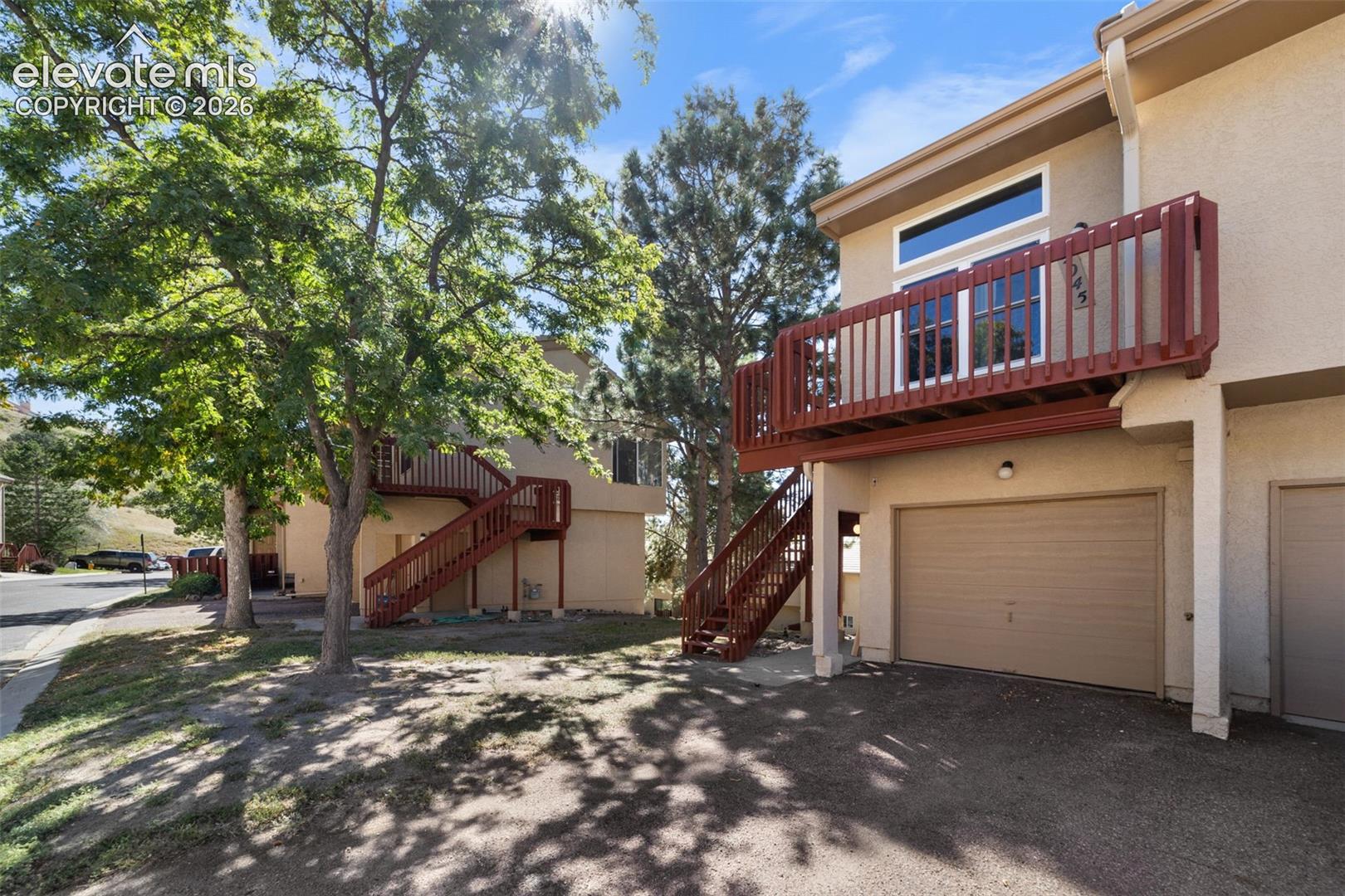 Stucco exterior featuring a private upper-level balcony with wood railing, attached garage, and staircase