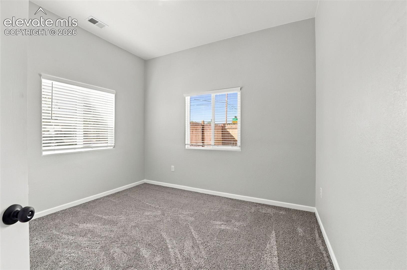 Neutral-toned walls, grey carpeting, and two windows with blinds