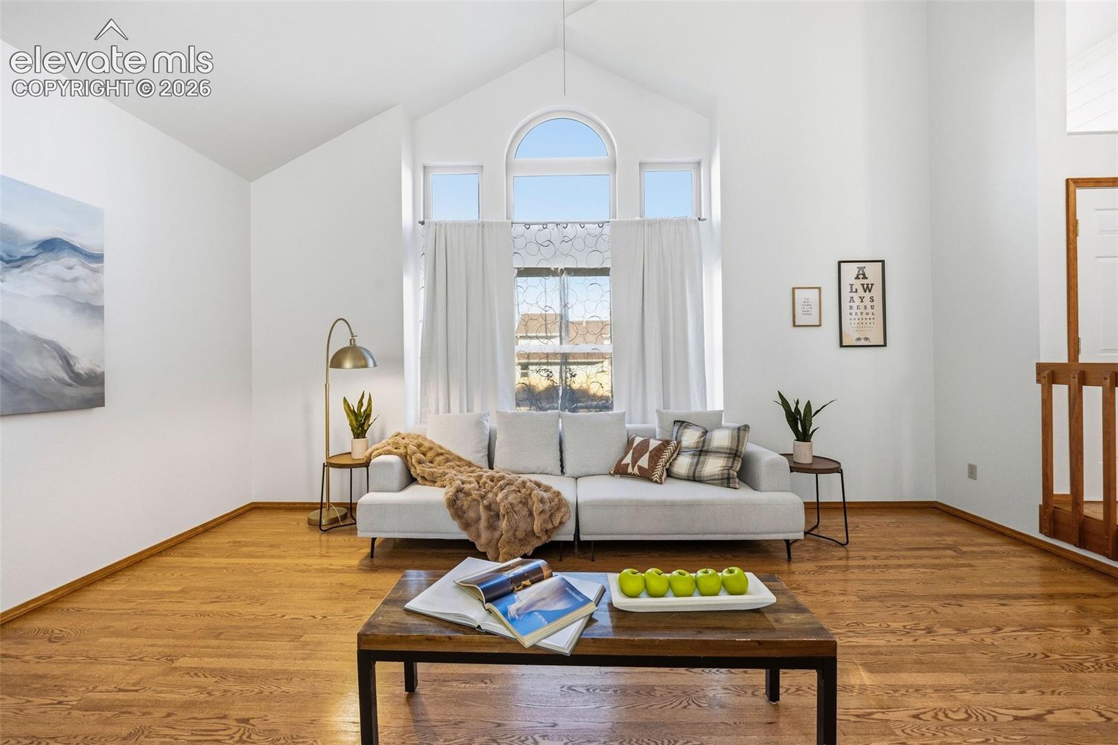 Vaulted ceiling featuring a prominent arched window, wood-finish flooring, and a decorative wood-slat railing