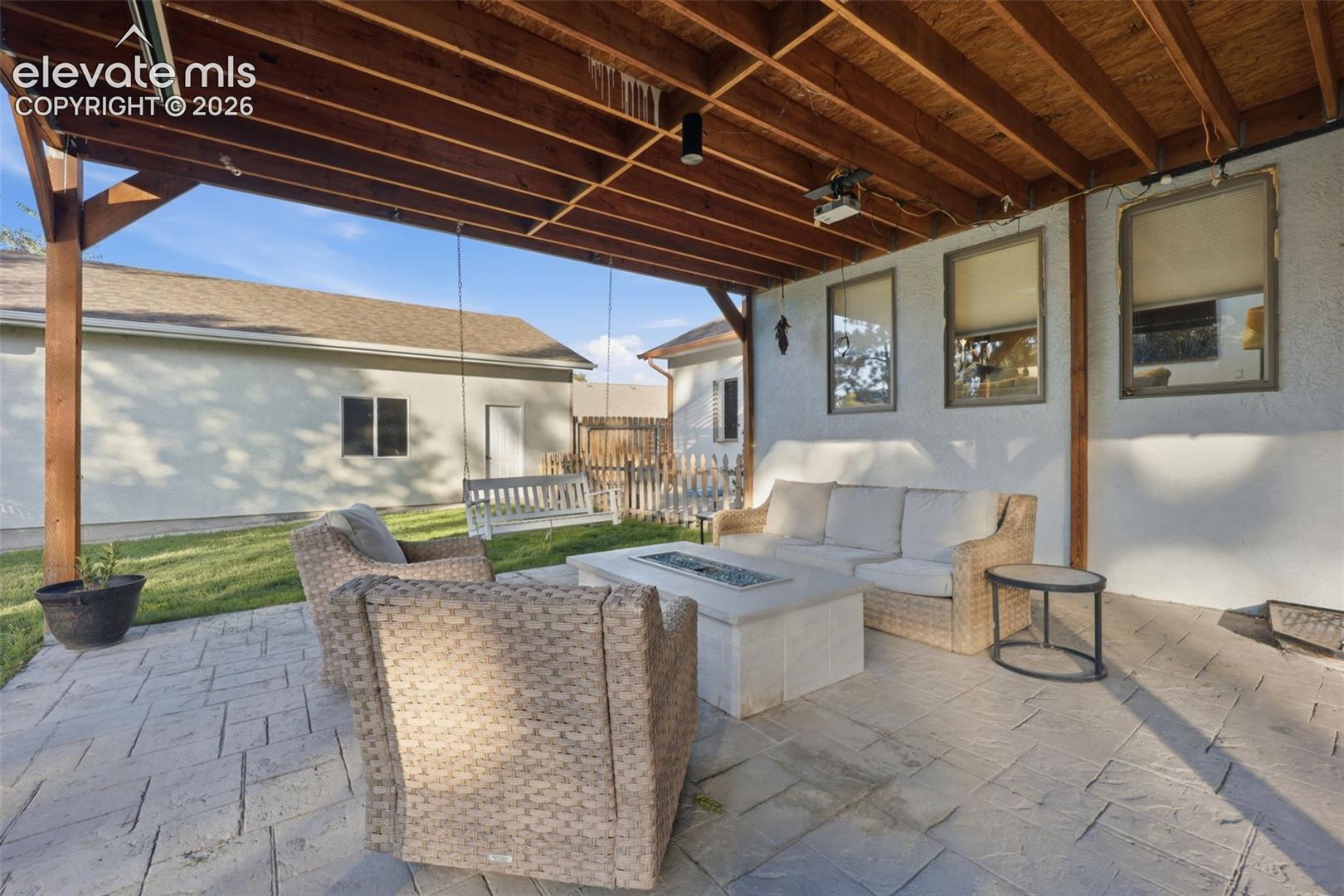 Covered patio with exposed wood beam ceiling, stamped concrete flooring, and a built-in fire pit