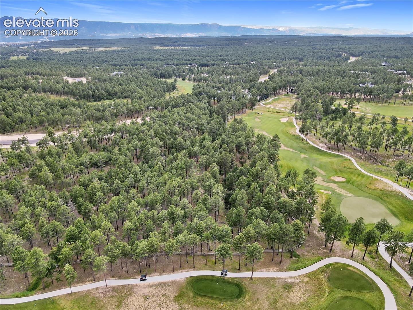 Aerial perspective of forested acreage featuring native evergreen trees, rolling terrain, mountain backdrops, and golf course fairways