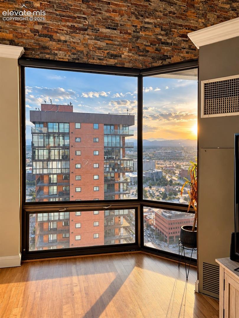 Corner window with expansive city scenery, wood-finish flooring, and a textured stone wall