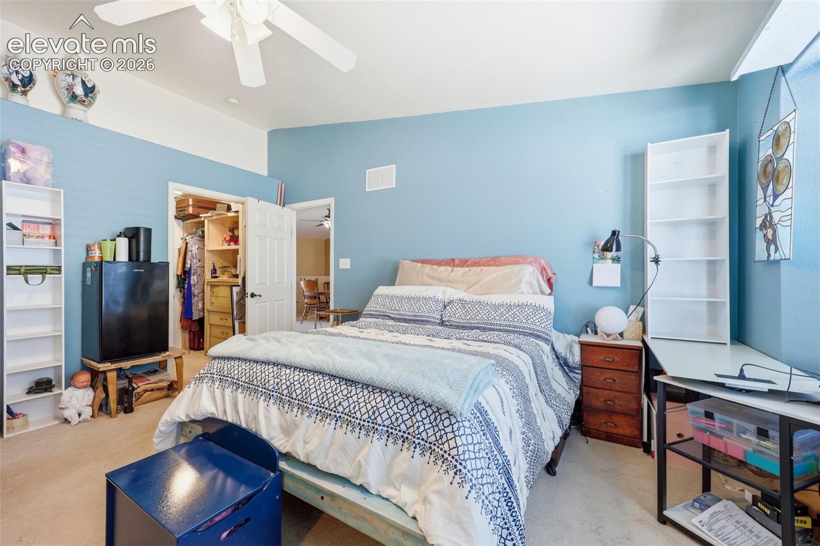 Carpeted bedroom featuring a ceiling fan, light blue walls, and a recessed closet with built-in shelving and drawers